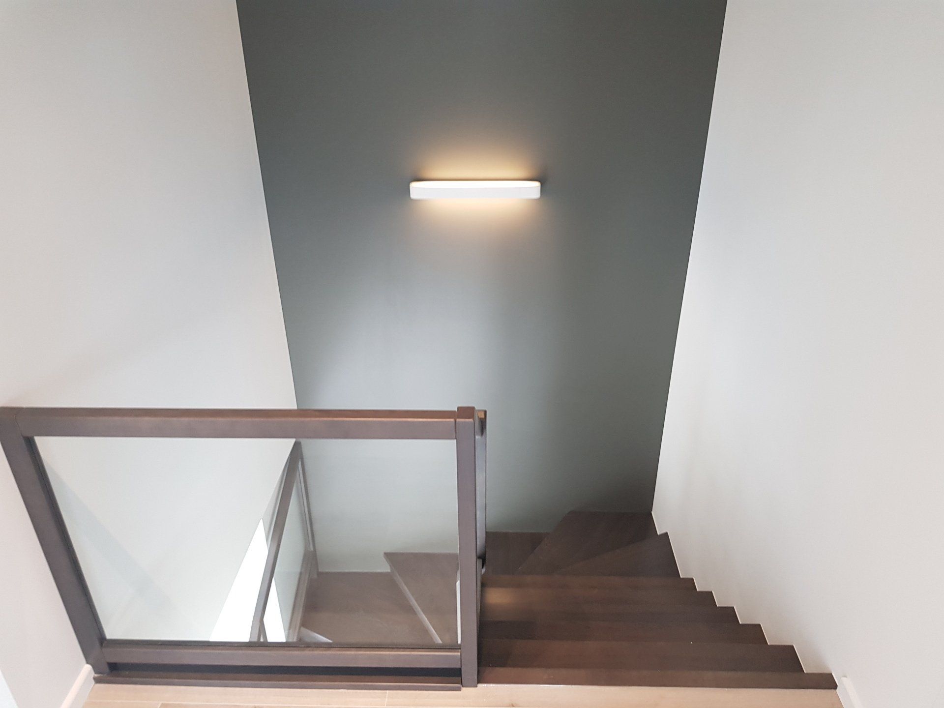 Laiptai su stikliniais turėklais ir šviesa ant sienos.