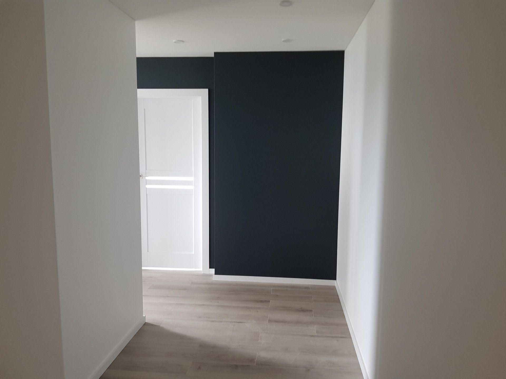 Tuščias koridorius su juoda siena ir baltomis durimis.