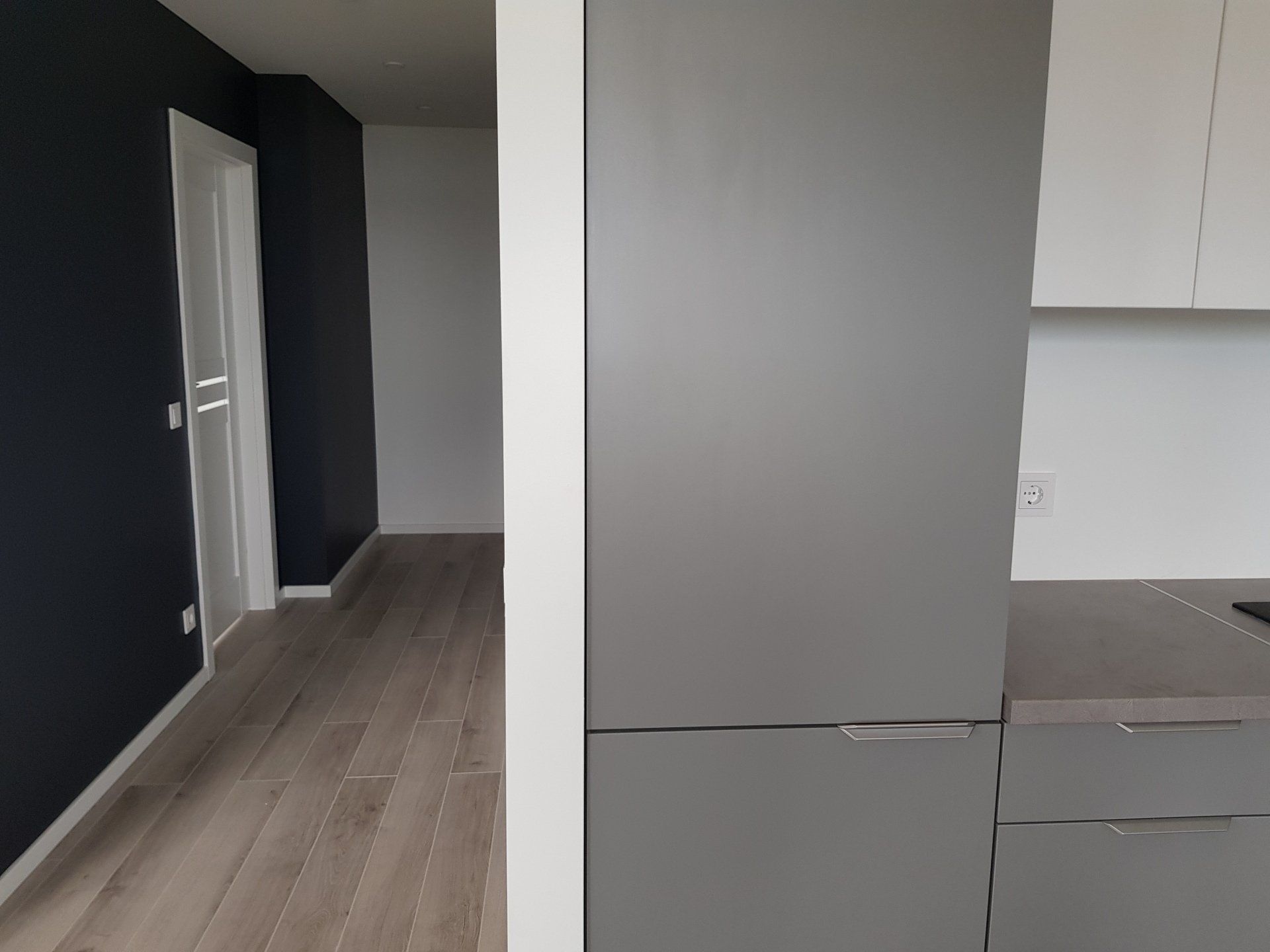 Virtuvė su pilku šaldytuvu ir baltomis spintelėmis