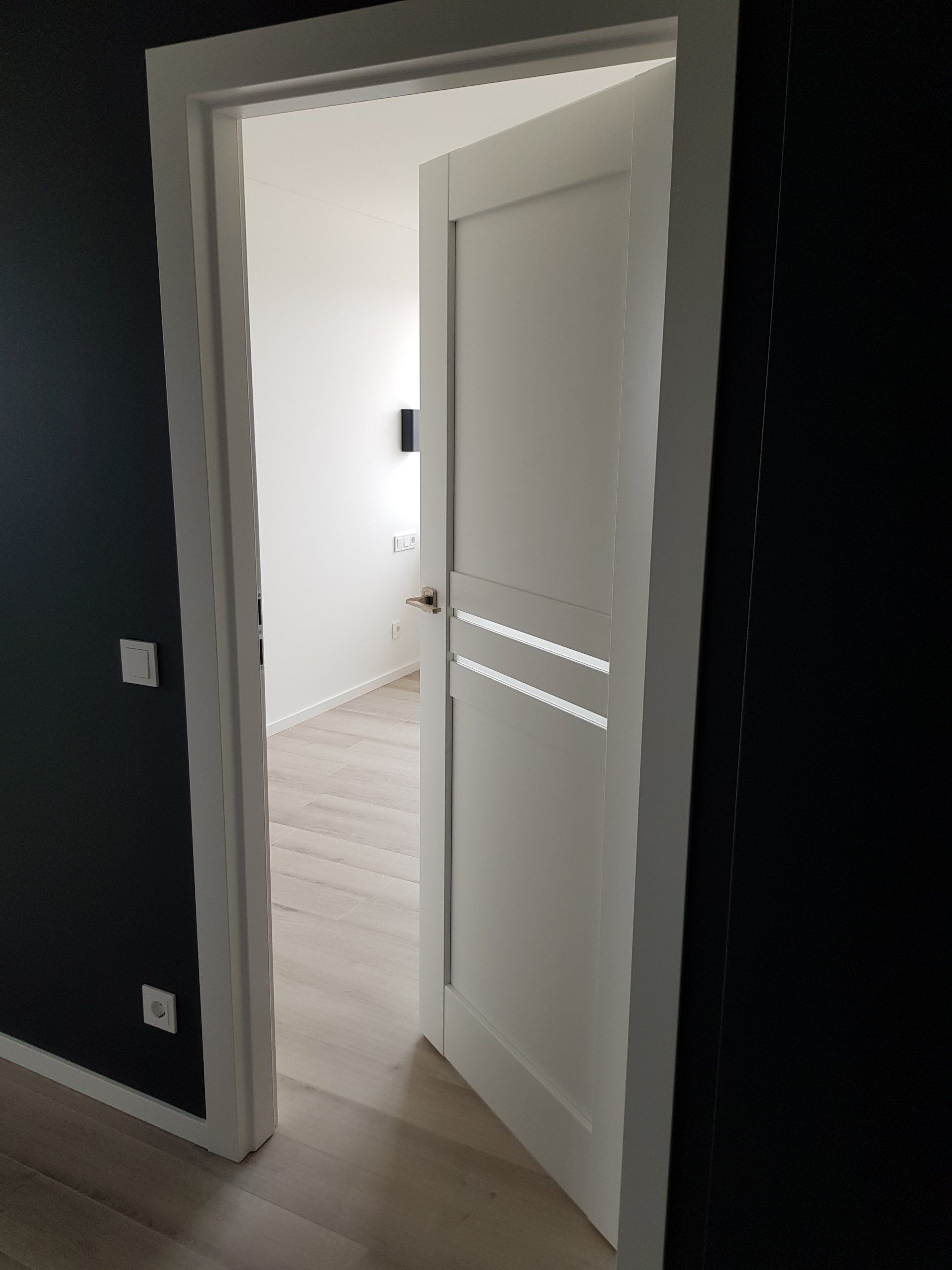Baltos durys veda į kambarį su juodomis sienomis.