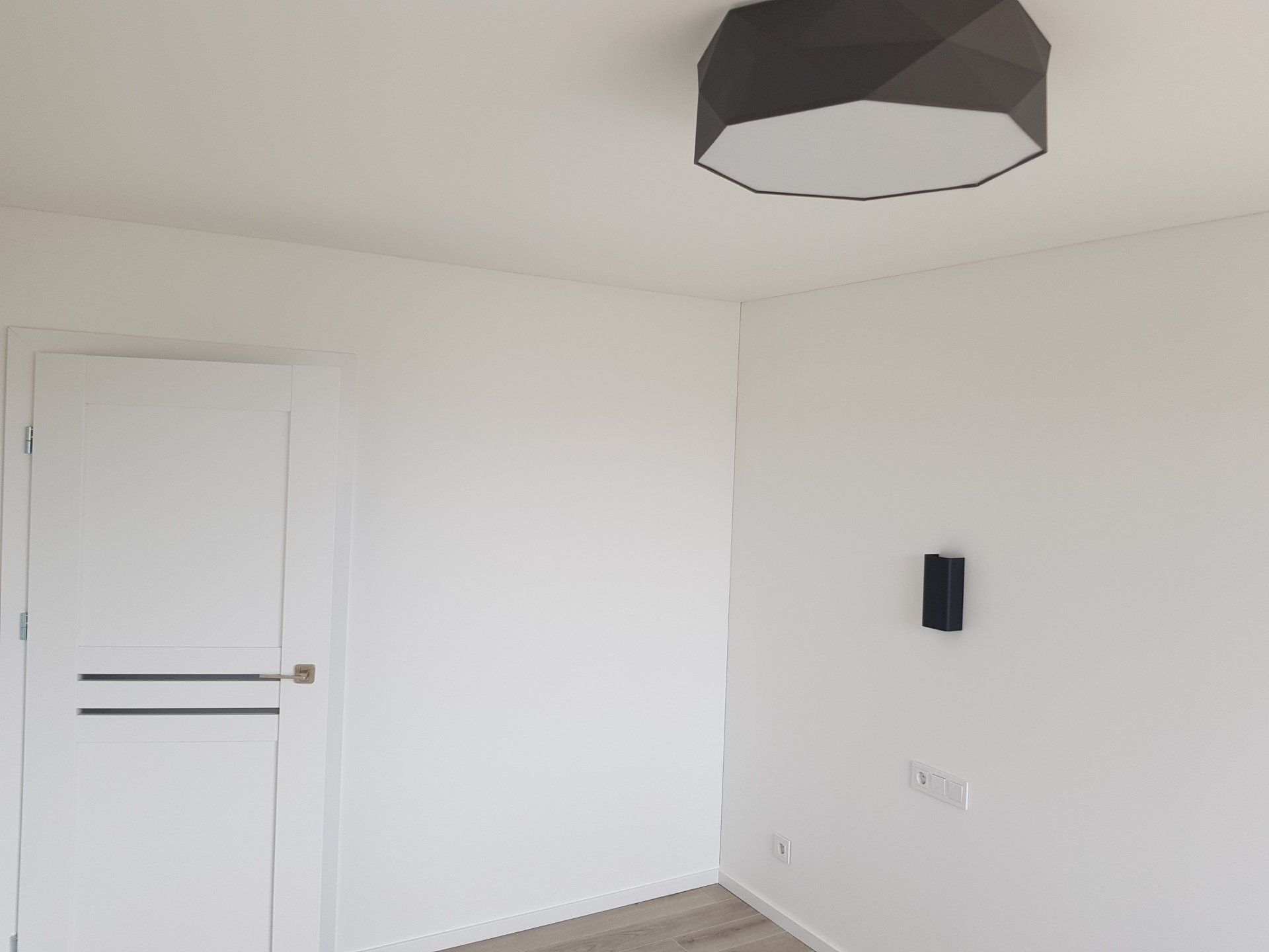 Tuščias kambarys su baltomis sienomis ir lubų šviestuvu