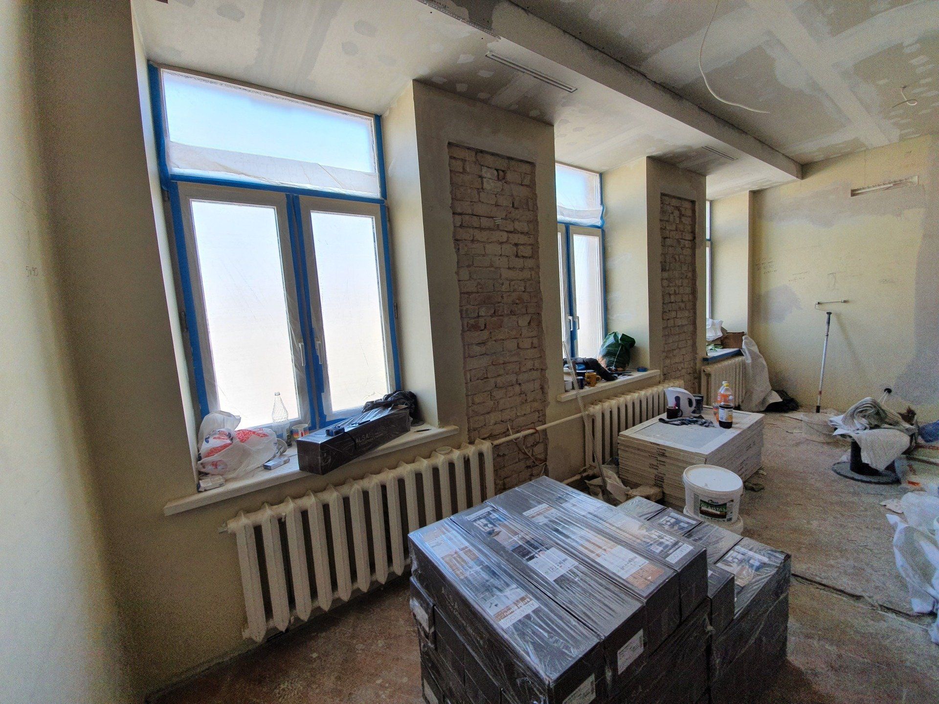 Kambarys su daugybe langų ir dėžių ant grindų.