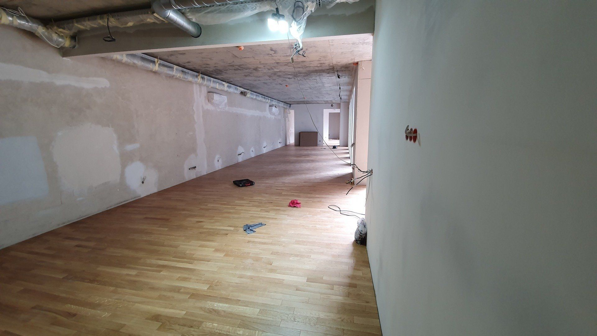 Tuščias kambarys su medinėmis grindimis ir baltomis sienomis.