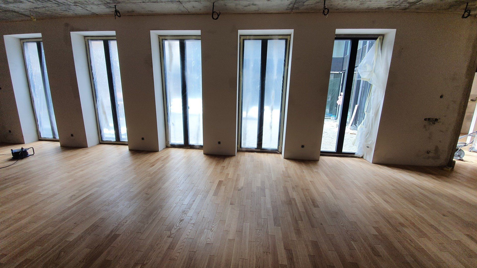 Didelis kambarys su medinėmis grindimis ir daugybe langų.