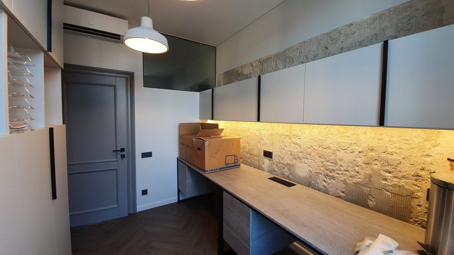 Virtuvė su kriaukle, spintelėmis ir plytų siena.