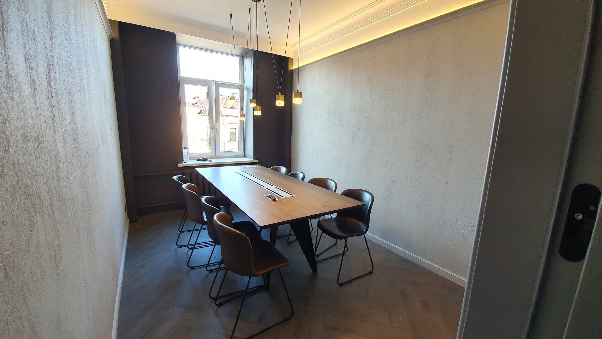 Konferencijų salė su ilgu stalu ir kėdėmis.