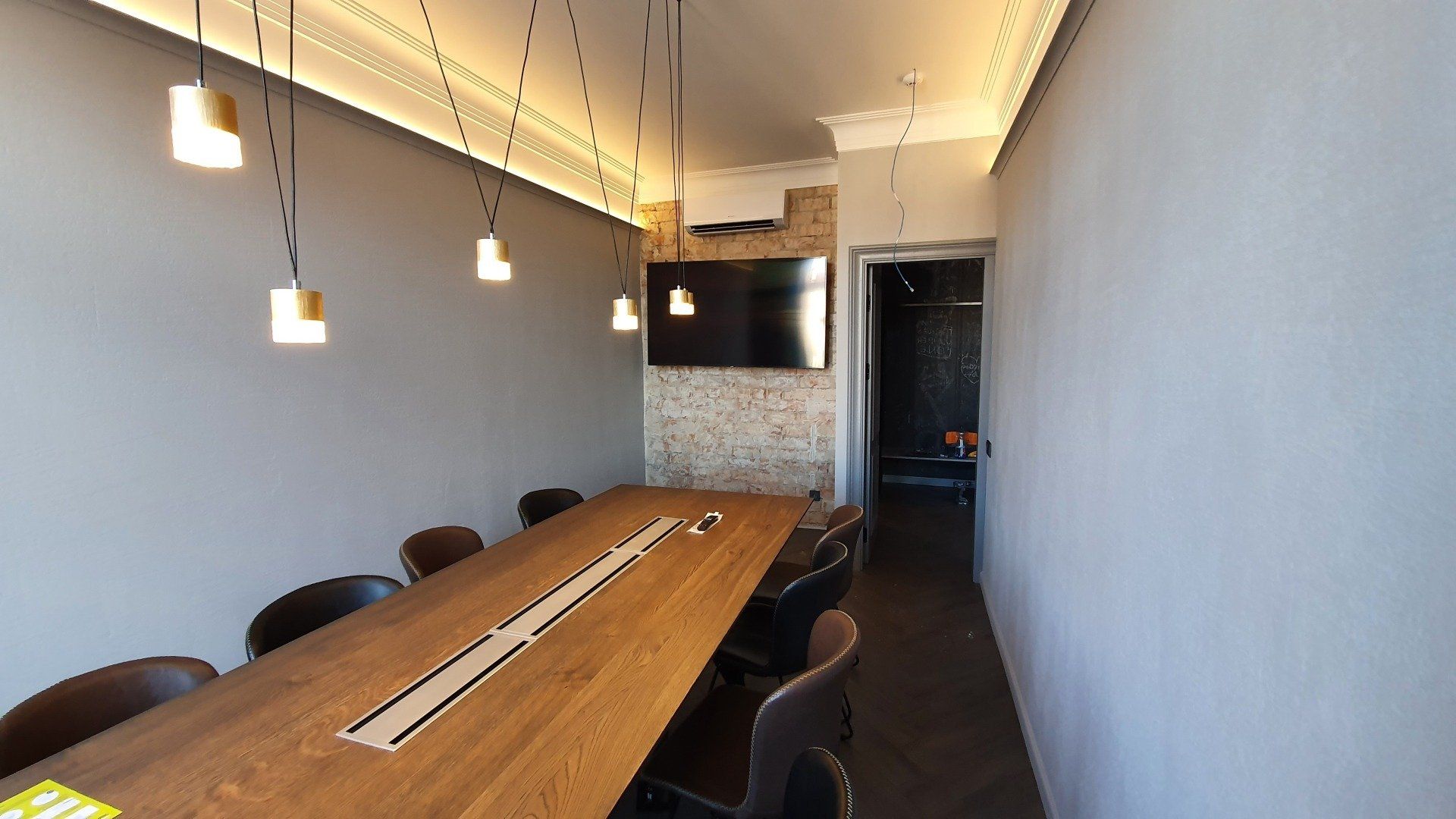 Konferencijų salė su ilgu mediniu stalu ir kėdėmis.