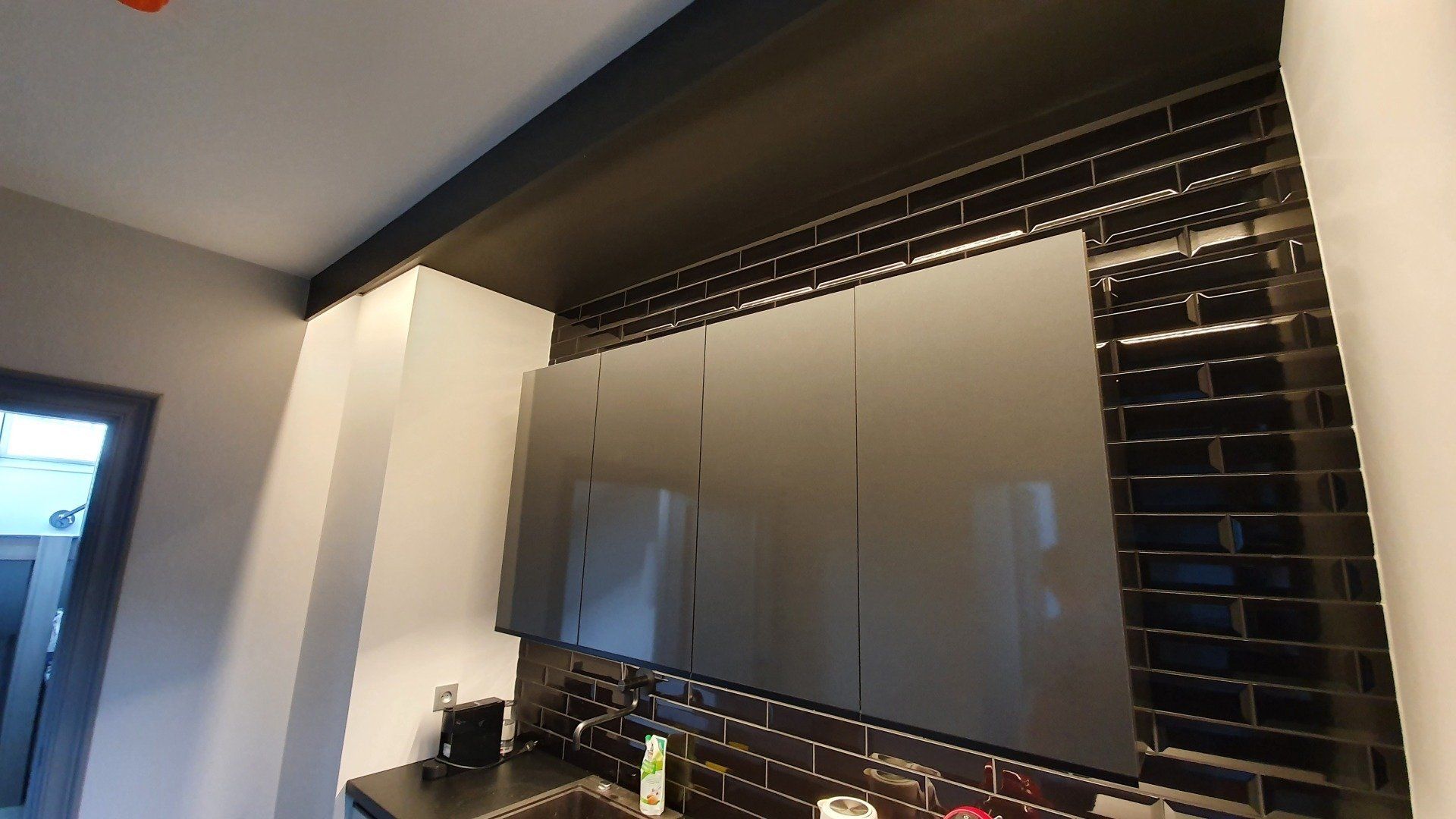 Virtuvė su juodomis spintelėmis ir juodomis metro plytelėmis.