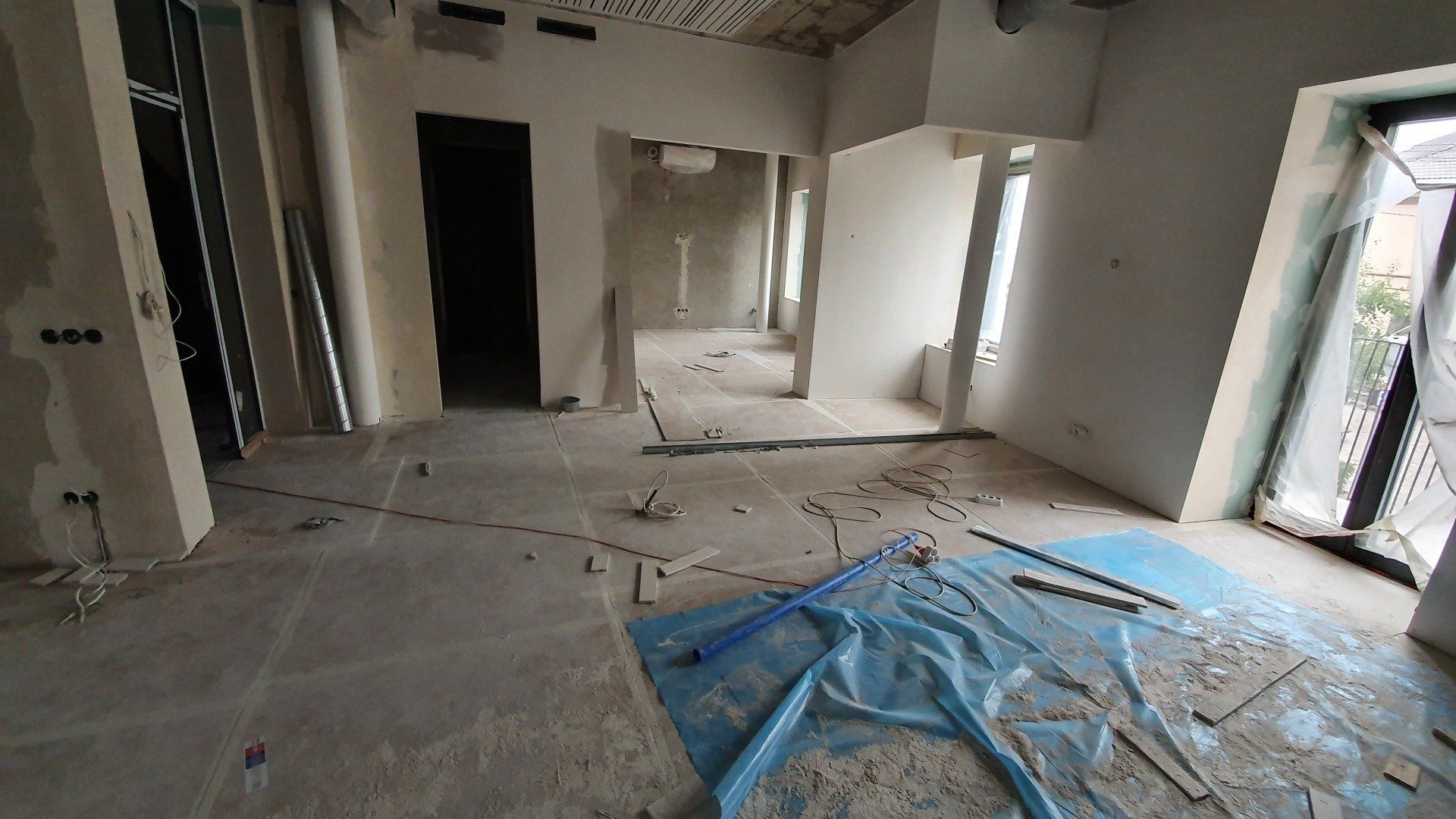 Tuščias kambarys su mėlynu brezentu ant grindų.