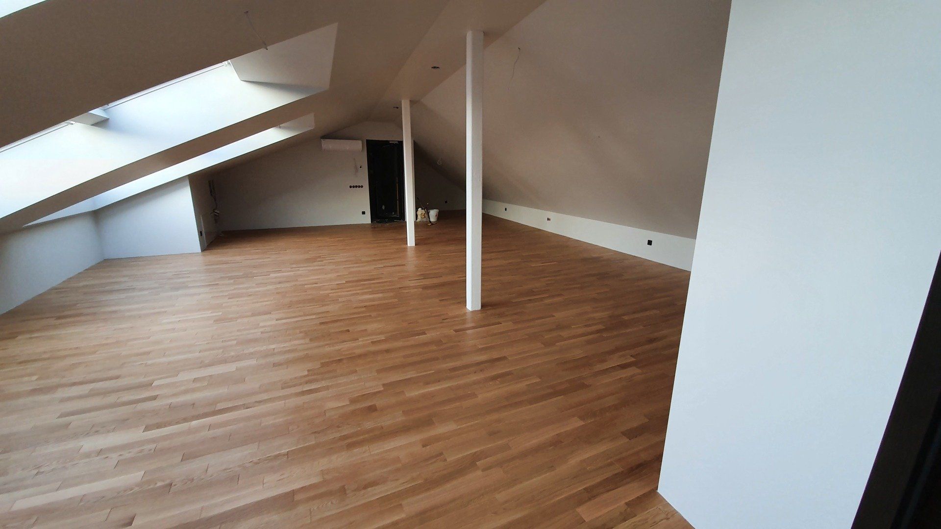 Tuščia palėpė su medinėmis grindimis ir baltomis sienomis.