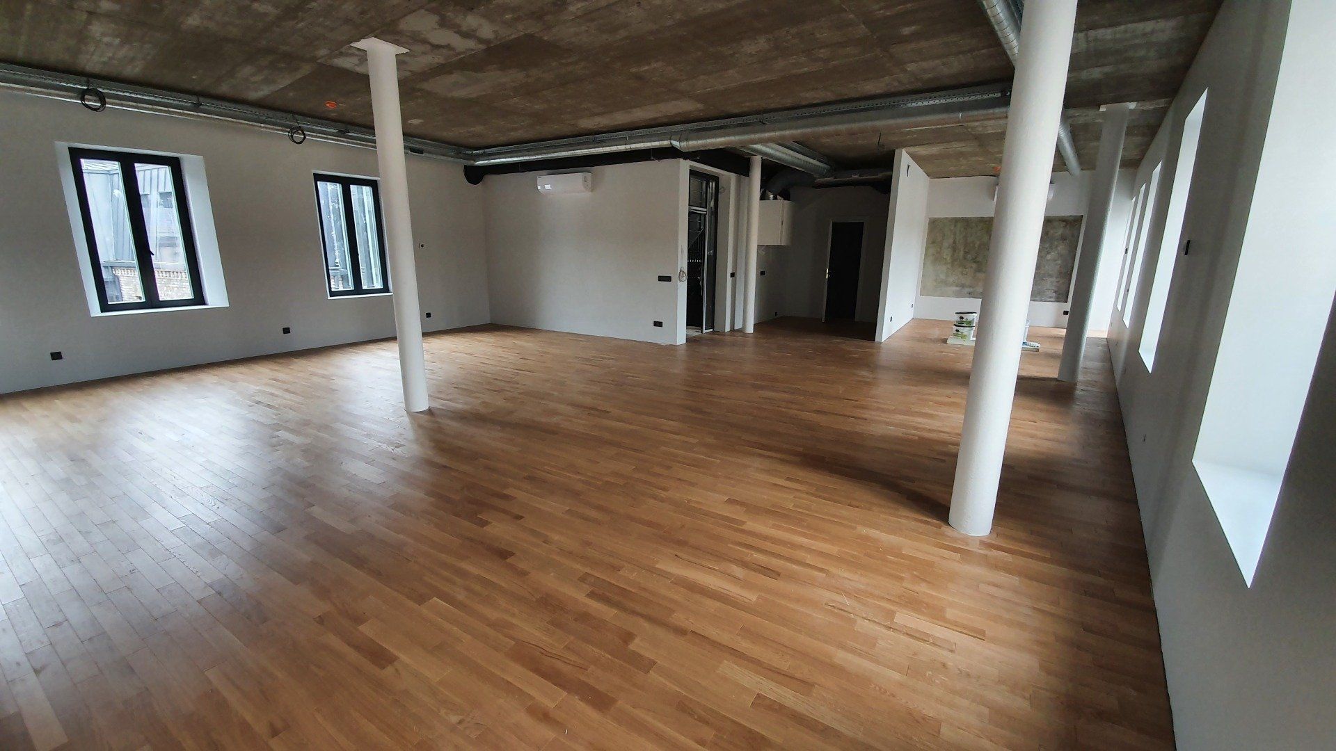 Didelis tuščias kambarys su medinėmis grindimis ir baltomis sienomis