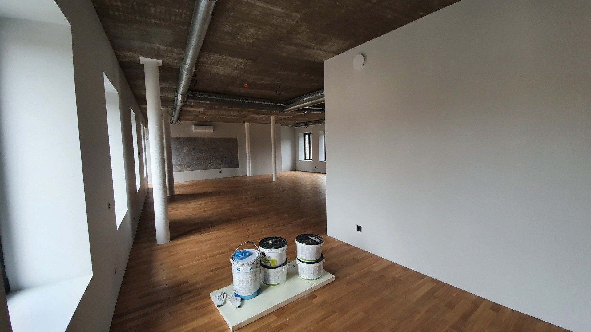 Tuščias kambarys su trimis kibirais dažų ant grindų.