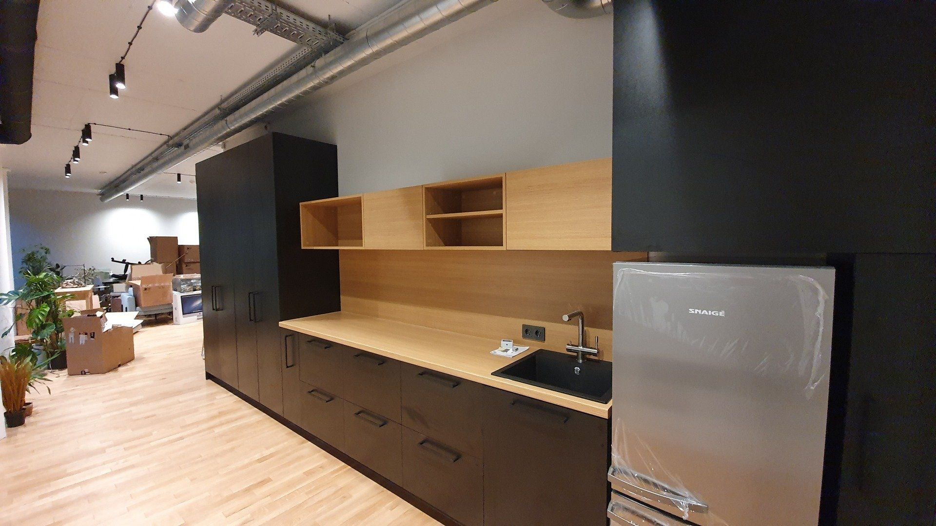 Virtuvė su juodomis spintelėmis, mediniais stalviršiais, kriaukle ir šaldytuvu.