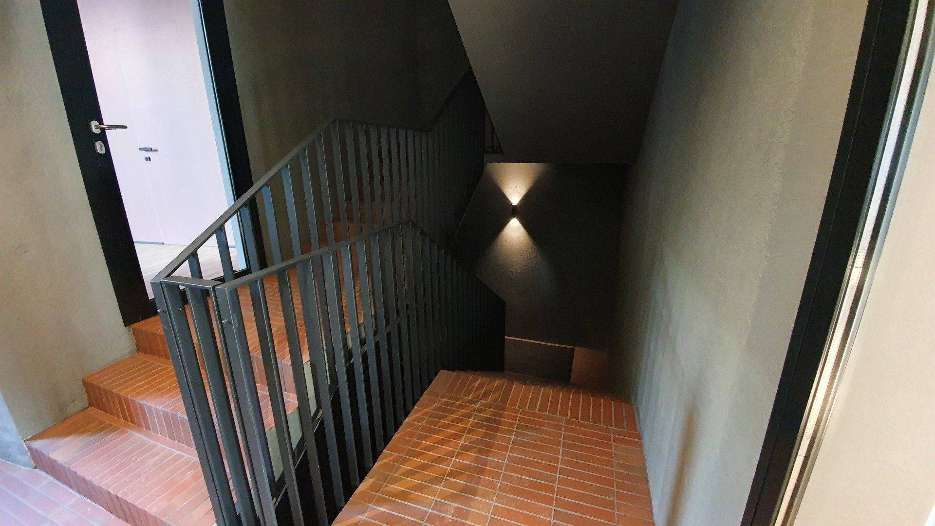 Laiptai su metaliniais turėklais, vedantys į antrą pastato aukštą.