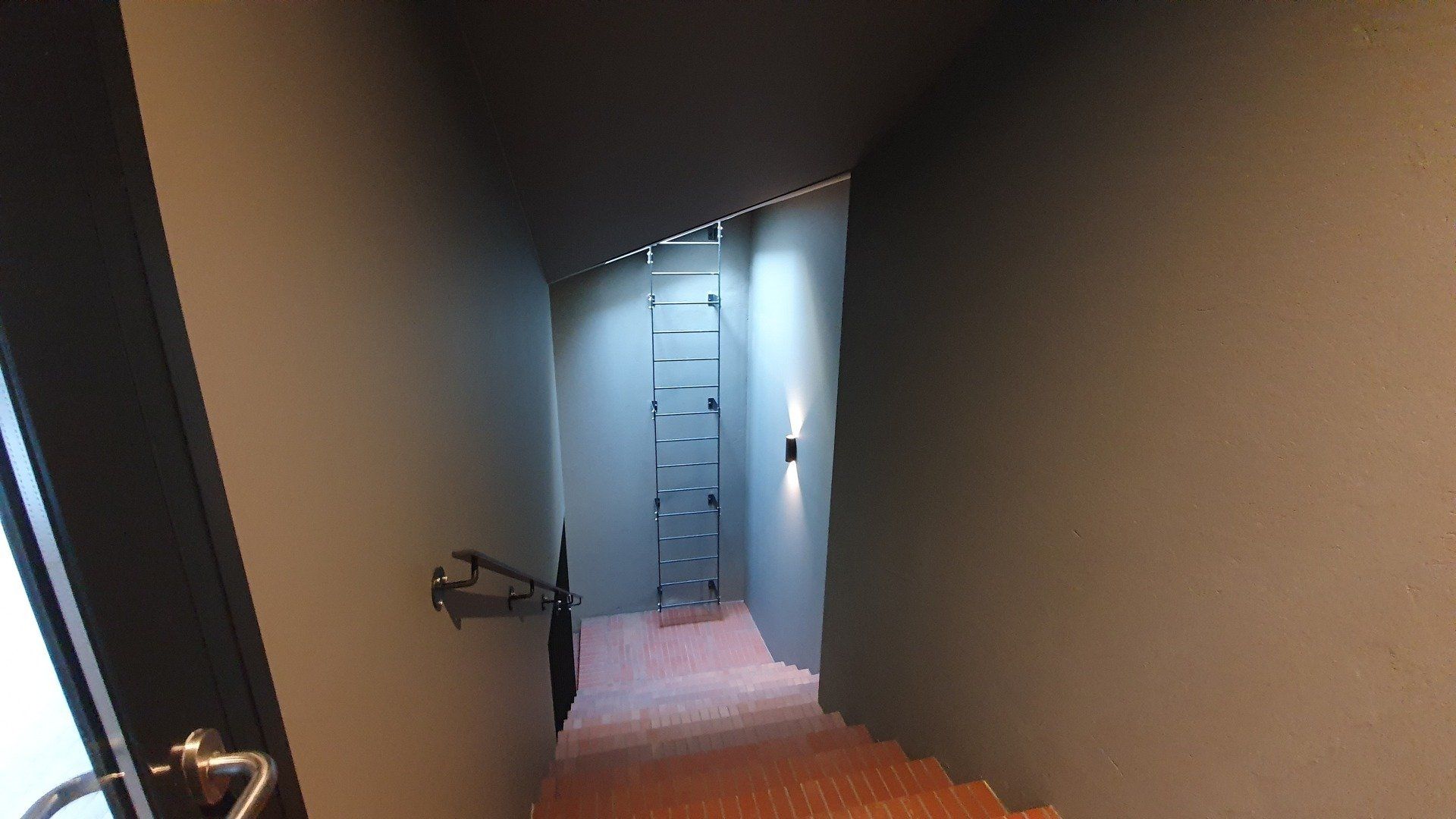 Ilgas koridorius su laiptais, vedančiais prie durų.