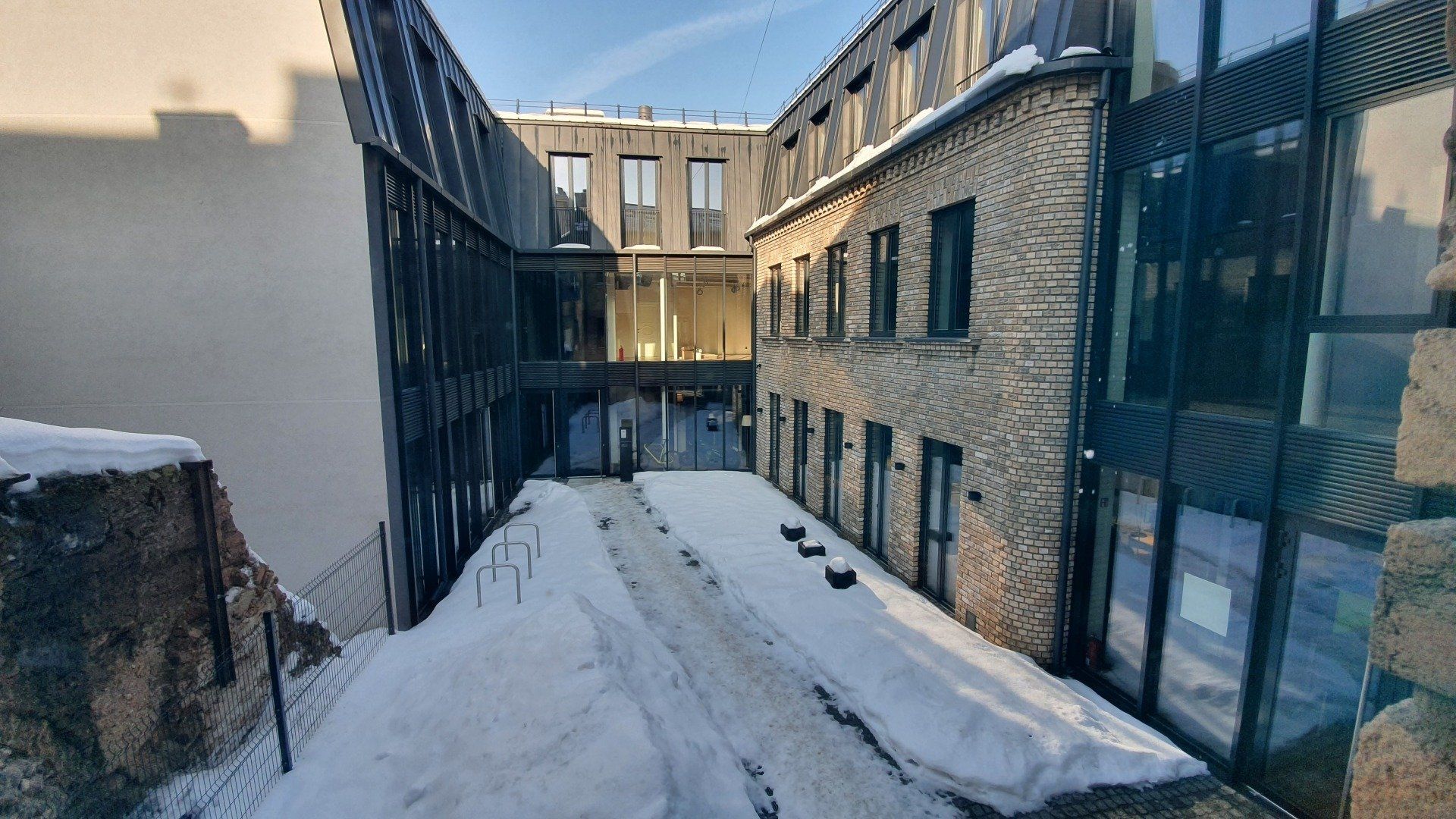 Snieguotas kiemas tarp dviejų pastatų saulėtą dieną.