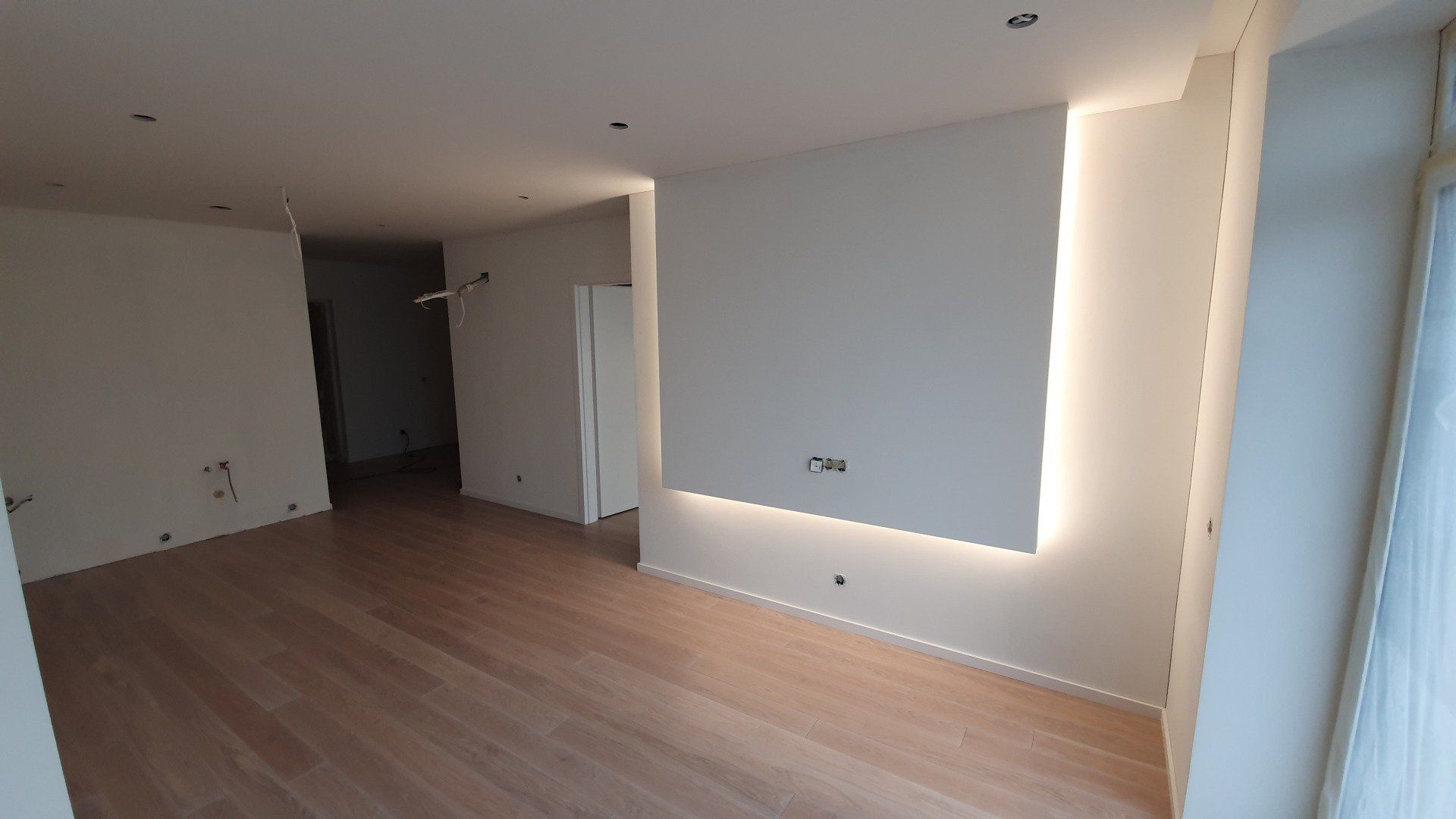 Tuščia svetainė su medinėmis grindimis ir baltomis sienomis.