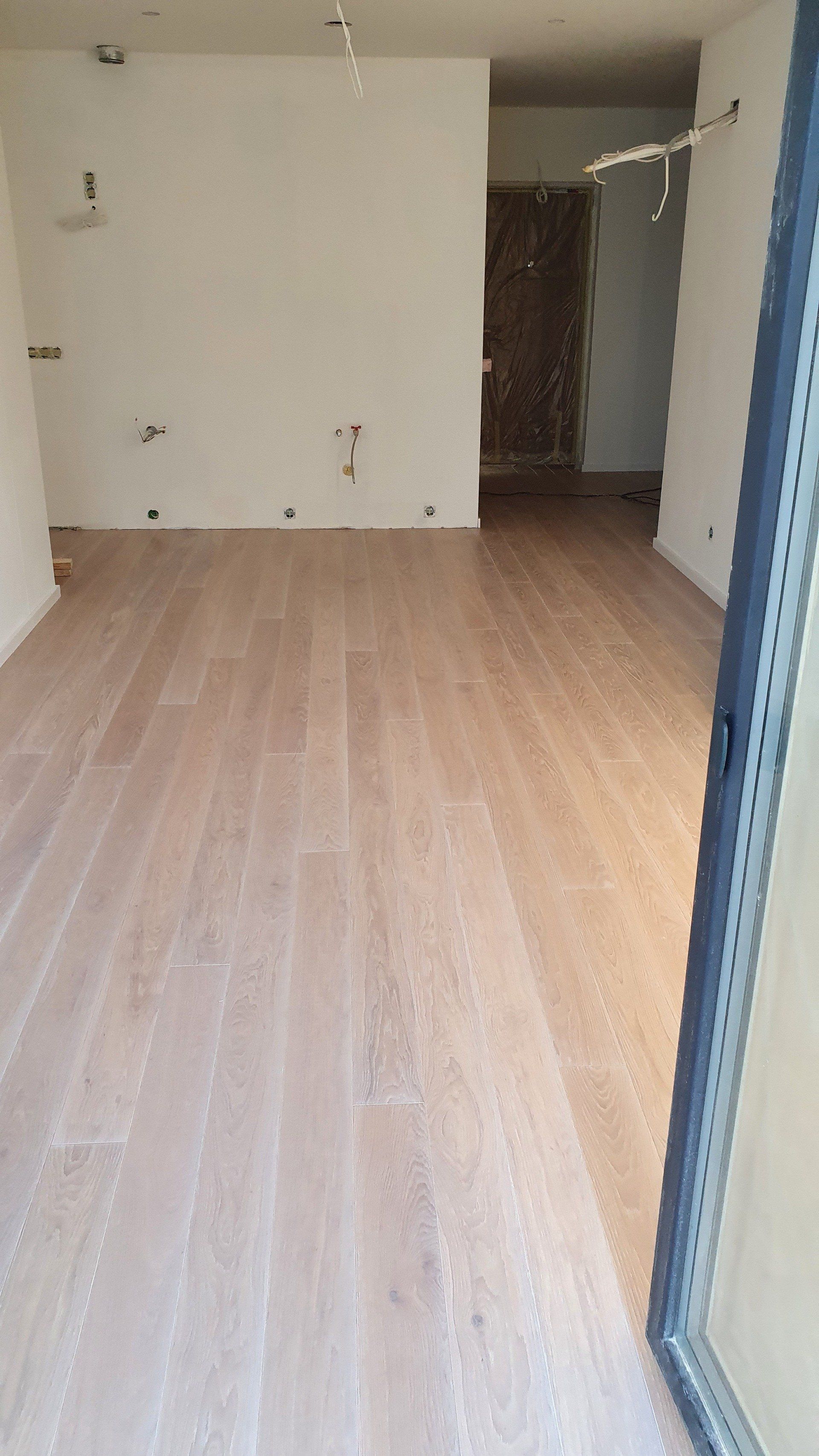 Tuščias kambarys su medinėmis grindimis ir baltomis sienomis.