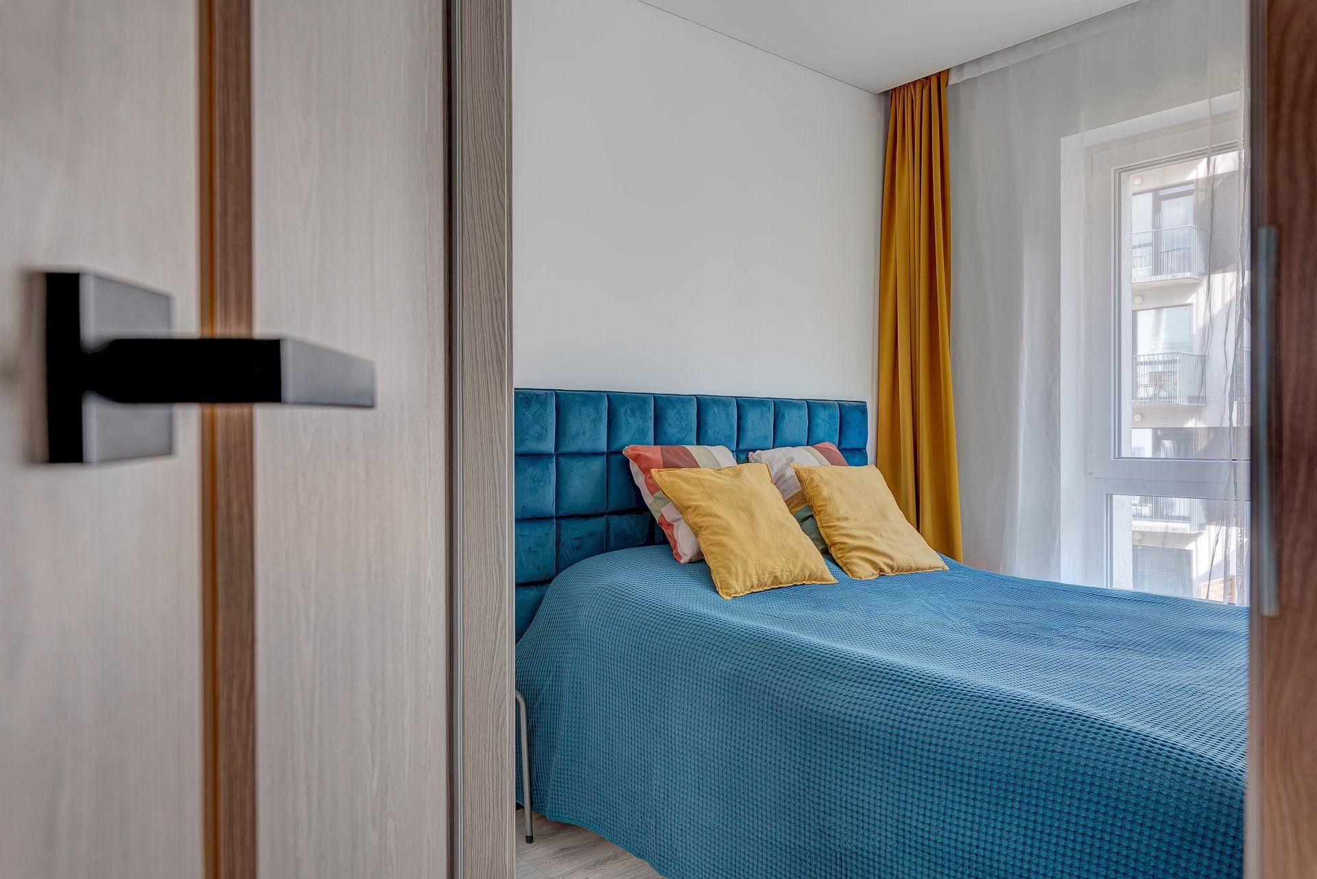 Miegamasis su mėlyna lova ir geltonomis užuolaidomis.