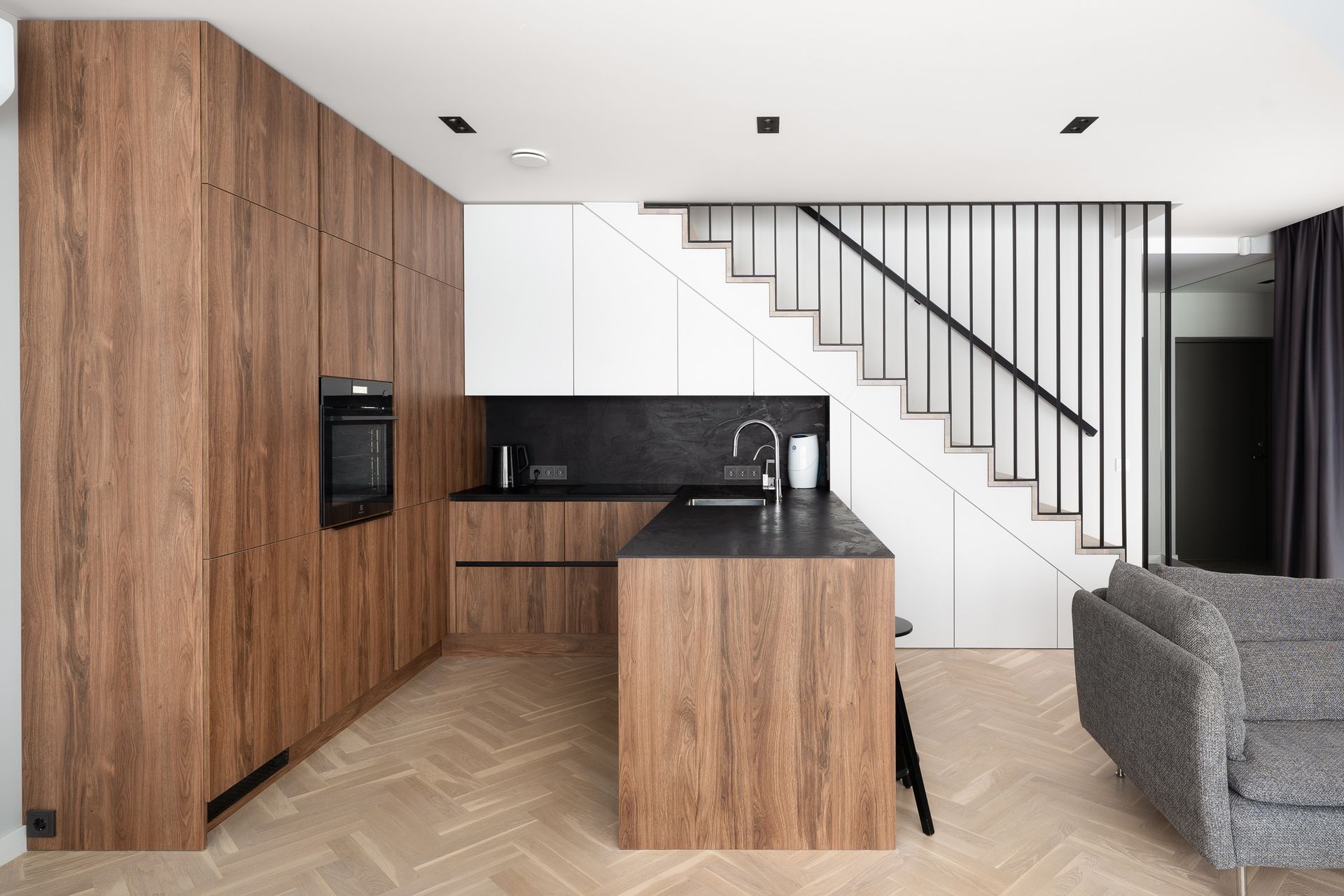 Virtuvė su medinėmis spintelėmis ir laiptais po jomis.