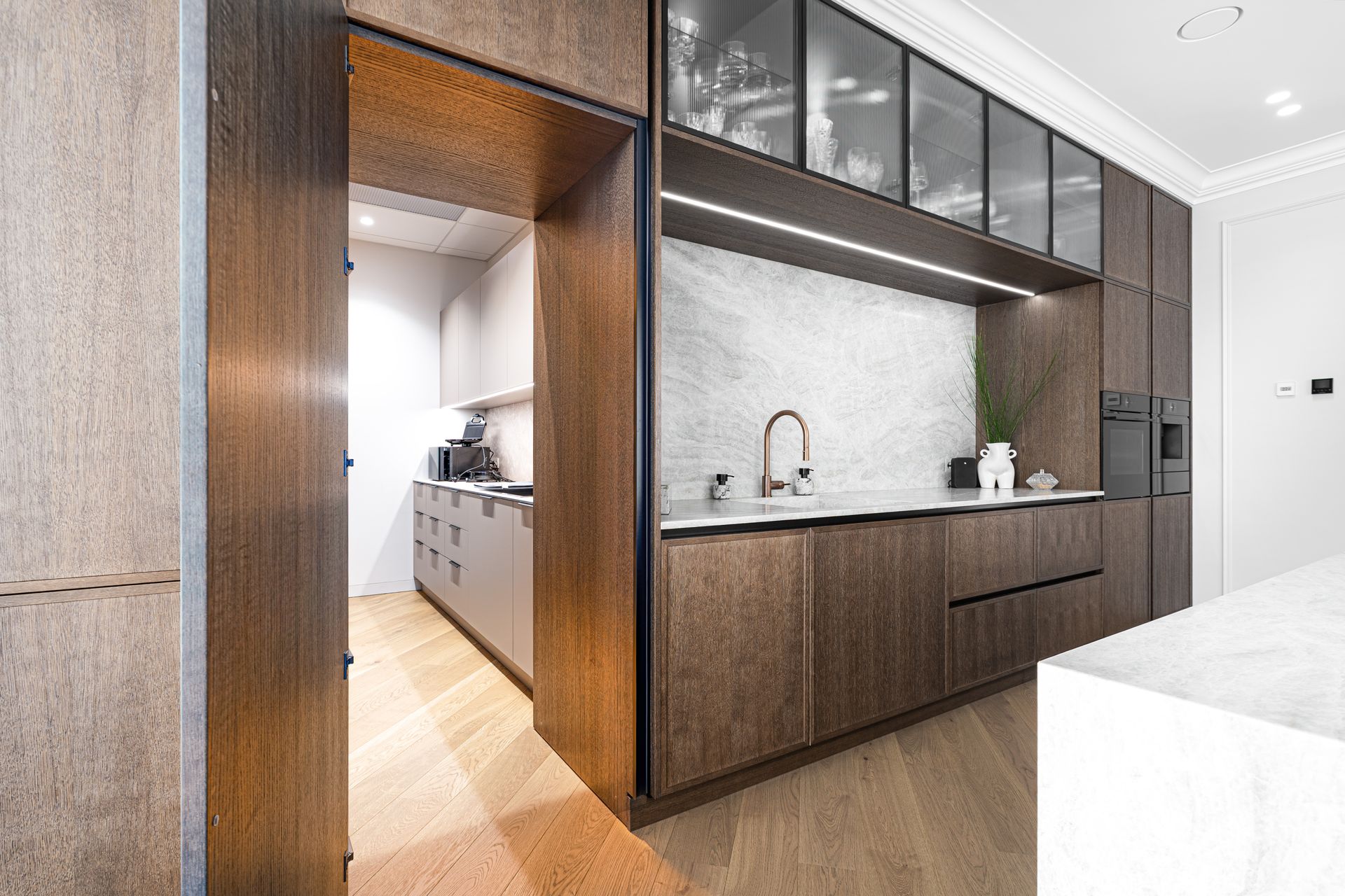 Modern kitchen with dark wood cabinetry, marble backsplash, and a hidden doorway.
