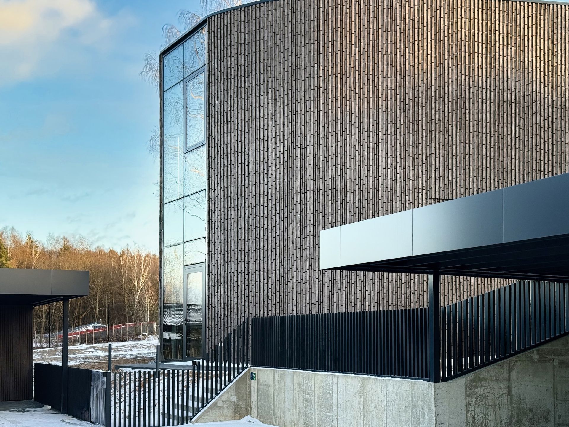 Modernus pastatas su mediniu fasadu ir į jį vedančiais laiptais.