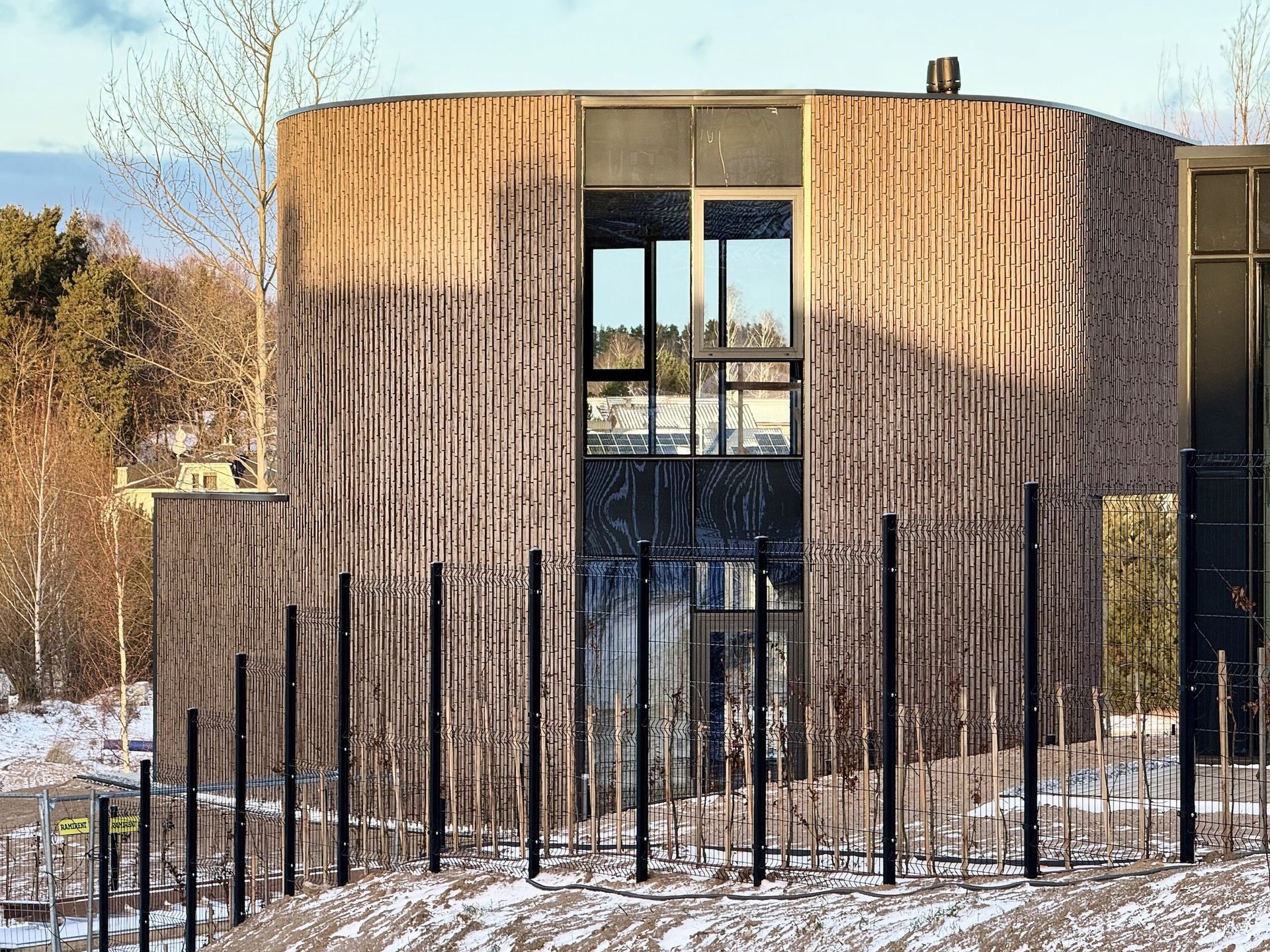 Didelis medinis pastatas su tvora aplink sniege.