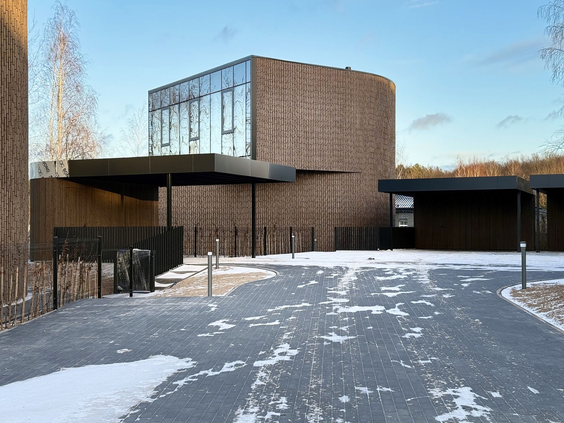 Didelis pastatas su daugybe langų yra apsuptas sniego ir medžių.