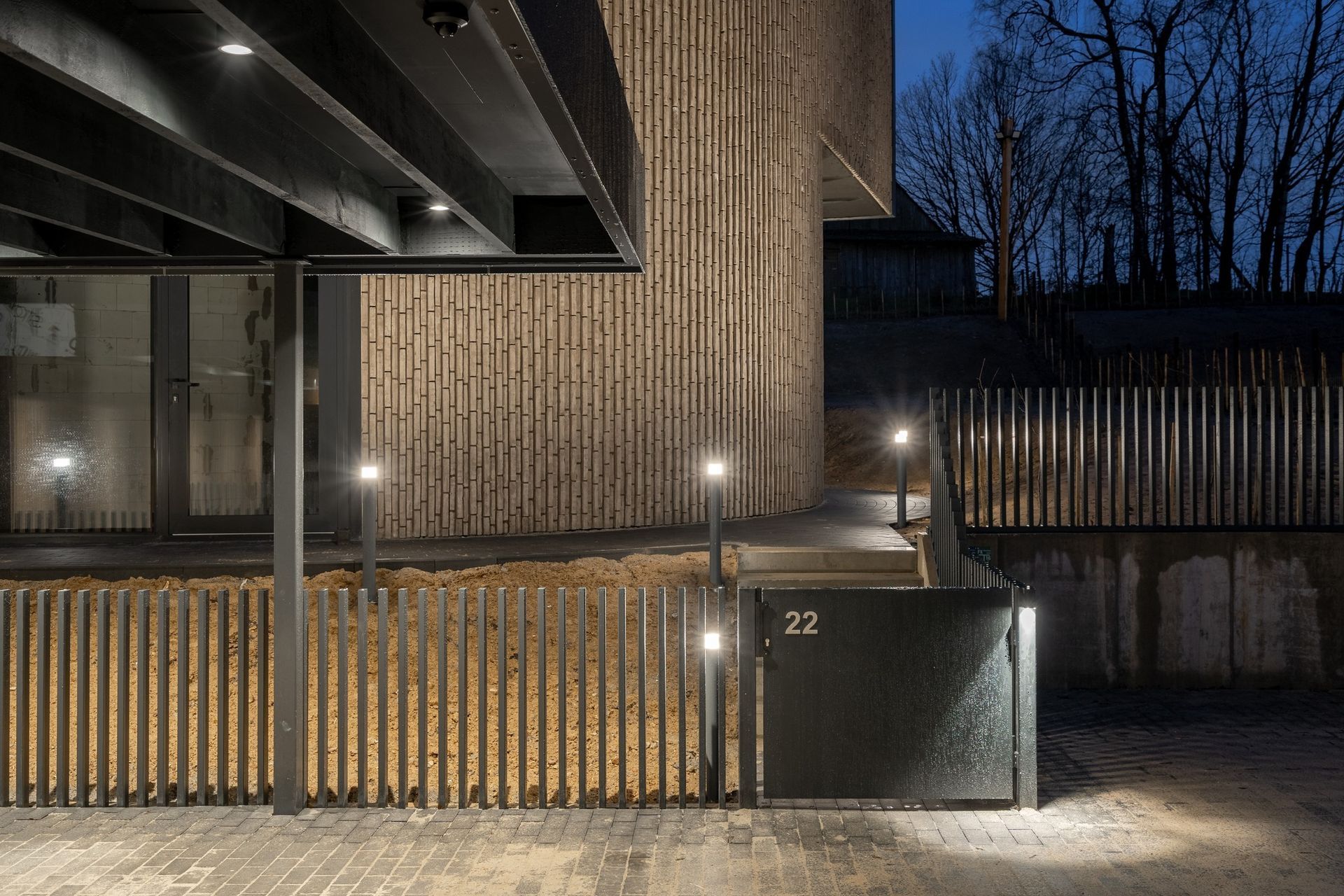 Pastatas su mediniu fasadu ir jį aptverta tvora naktį.