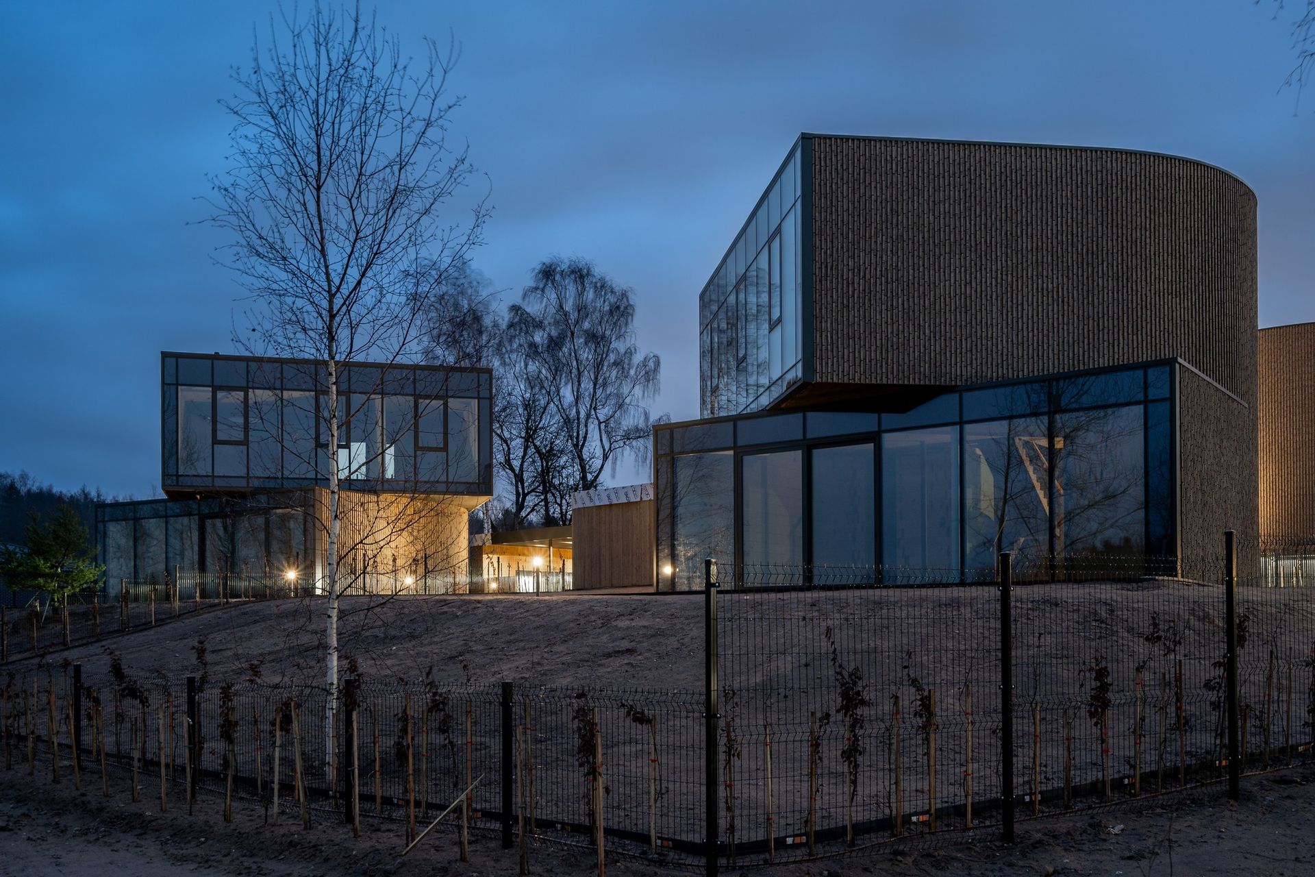 Didelis pastatas su daugybe langų yra apsuptas medžių ir tvoros.