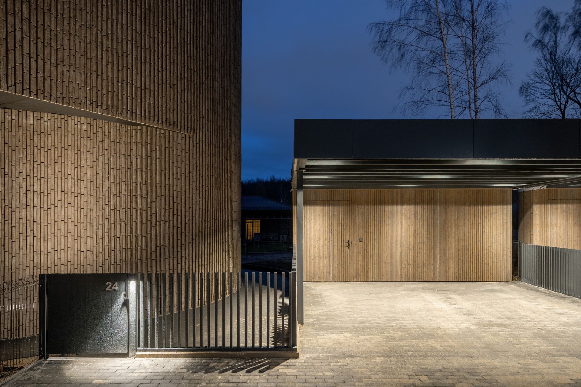 Yra garažas su mediniais vartais ir tvora priešais jį.