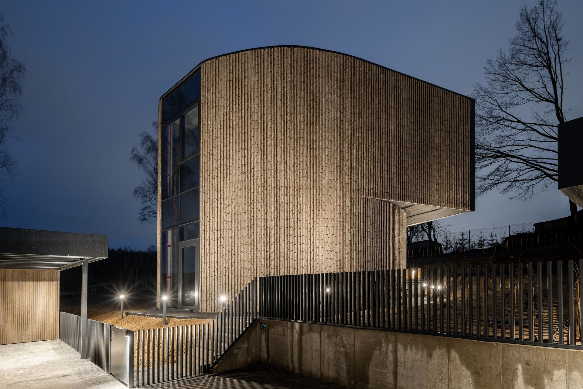 Naktį apšviestas didelis pastatas mediniu fasadu.