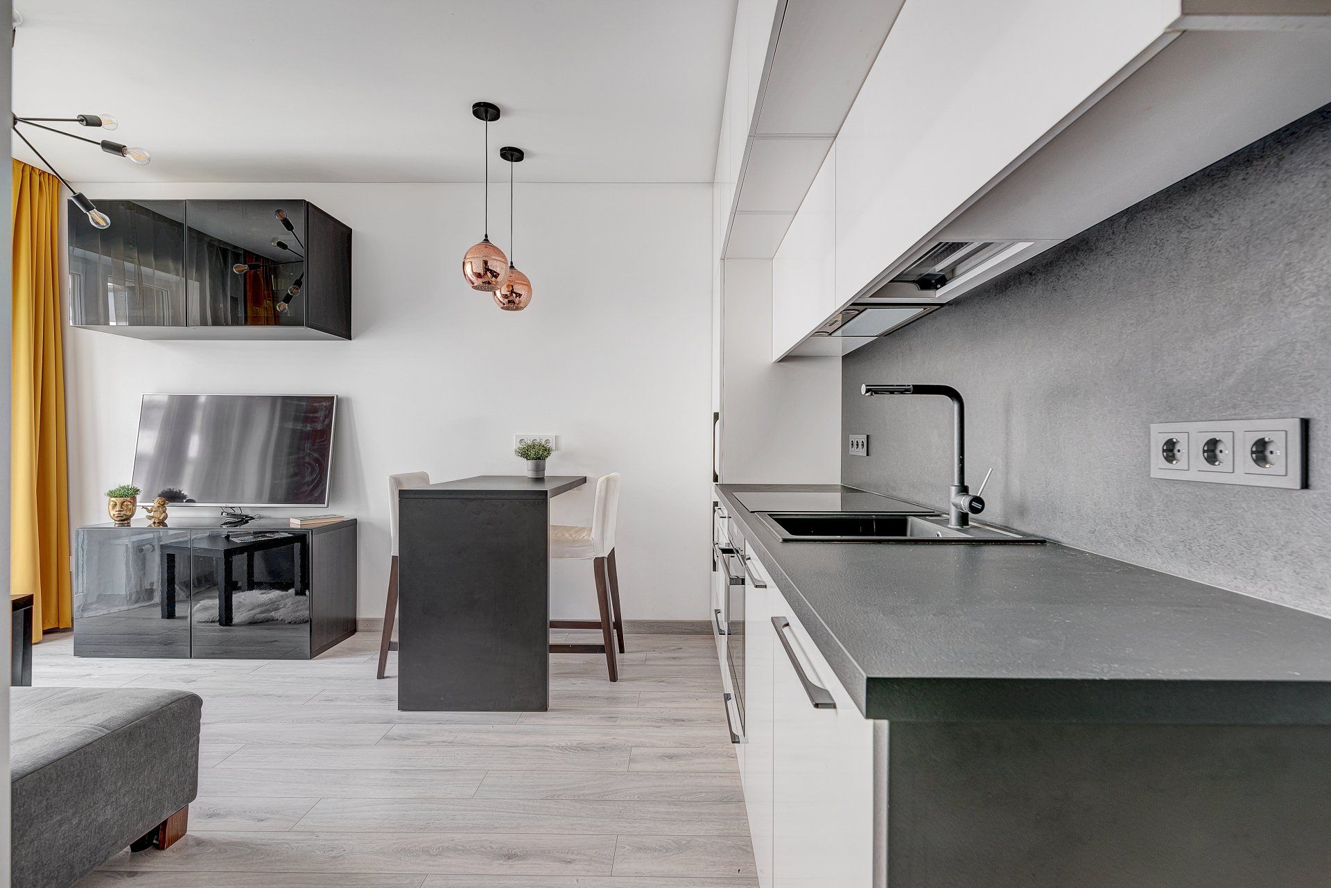 Virtuvė su kriaukle, spintelėmis ir televizoriumi.