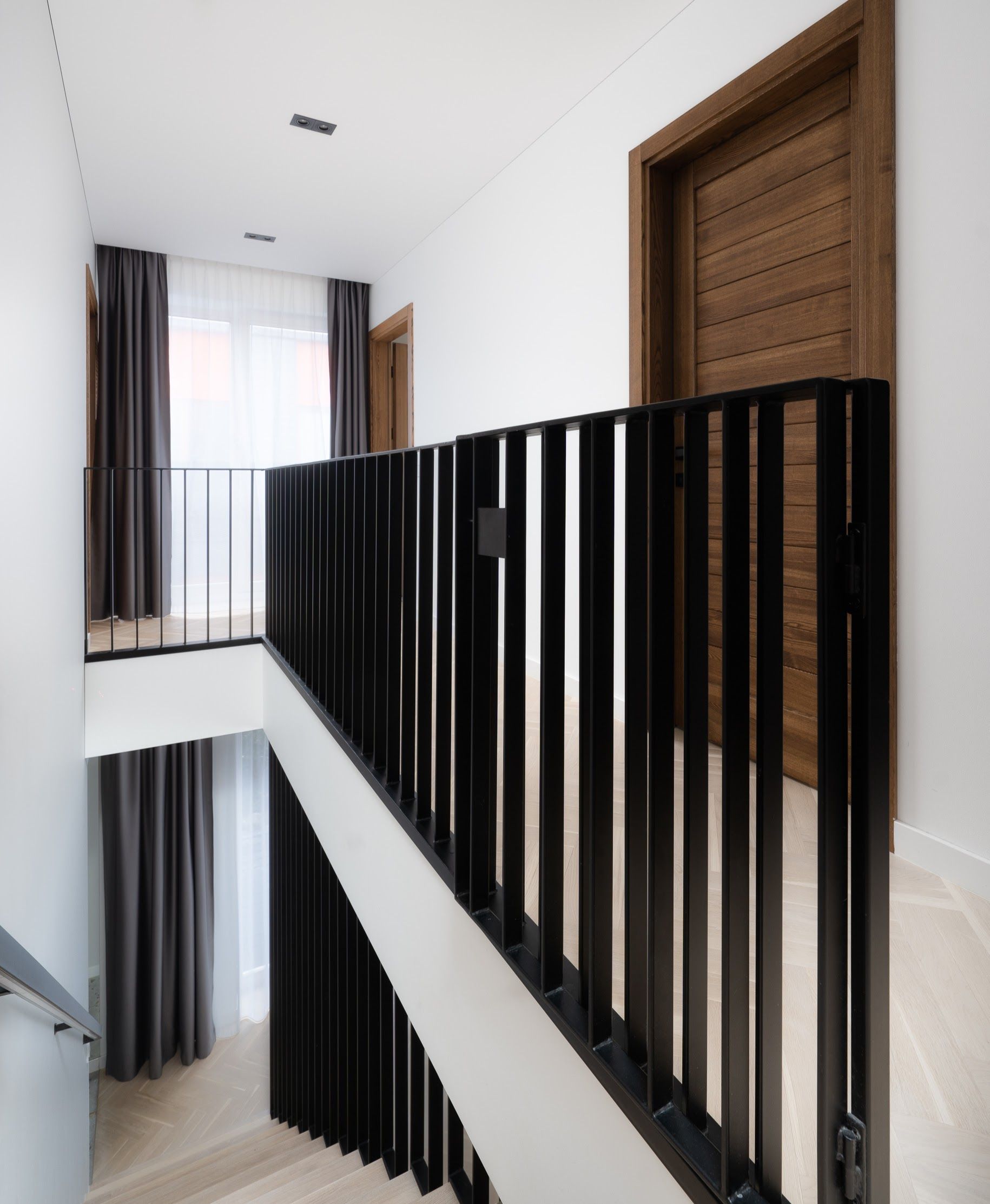 Laiptai su juodais turėklais ir medinėmis durimis