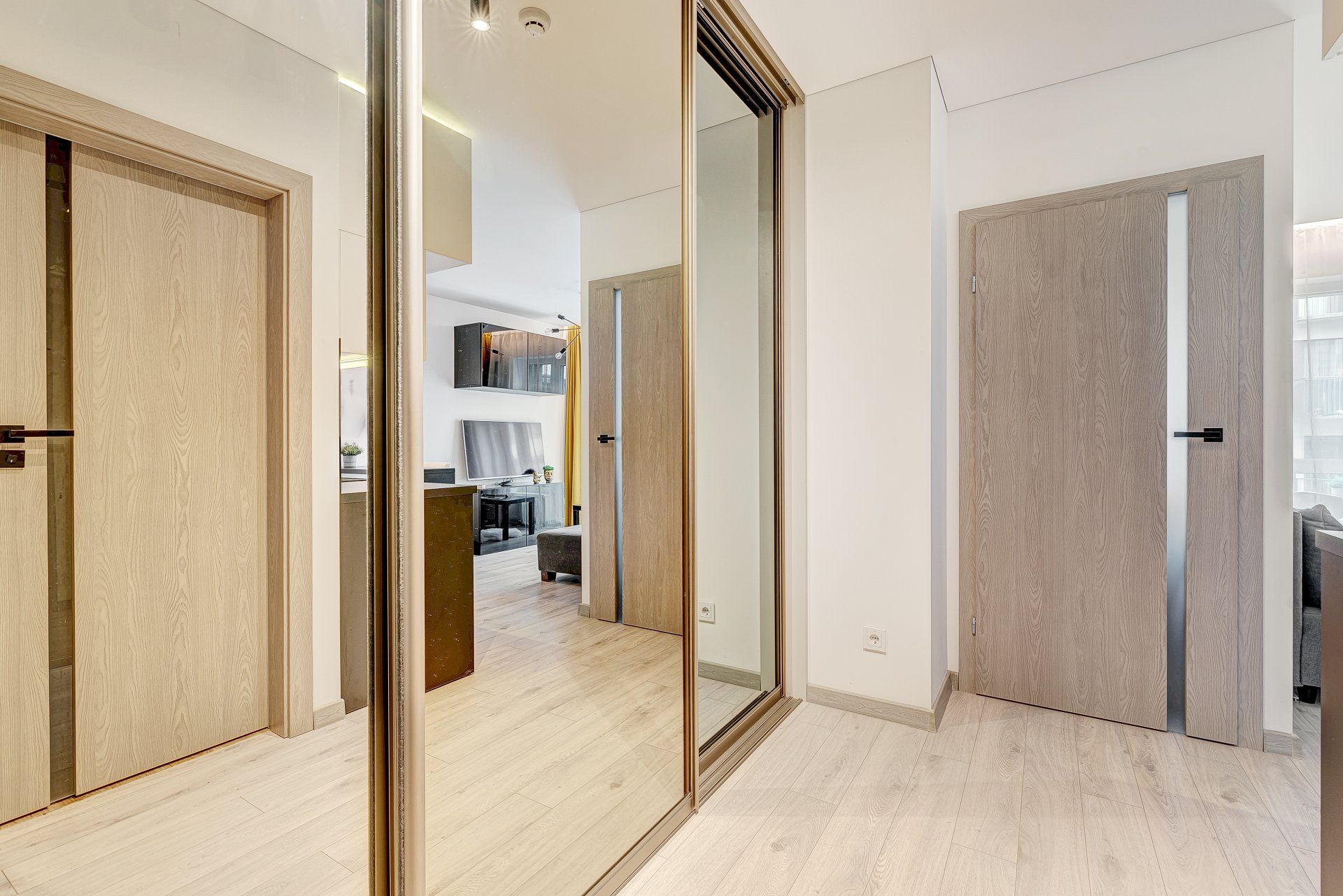 Koridorius su dideliu veidrodžiu ant sienos ir medinėmis durimis.