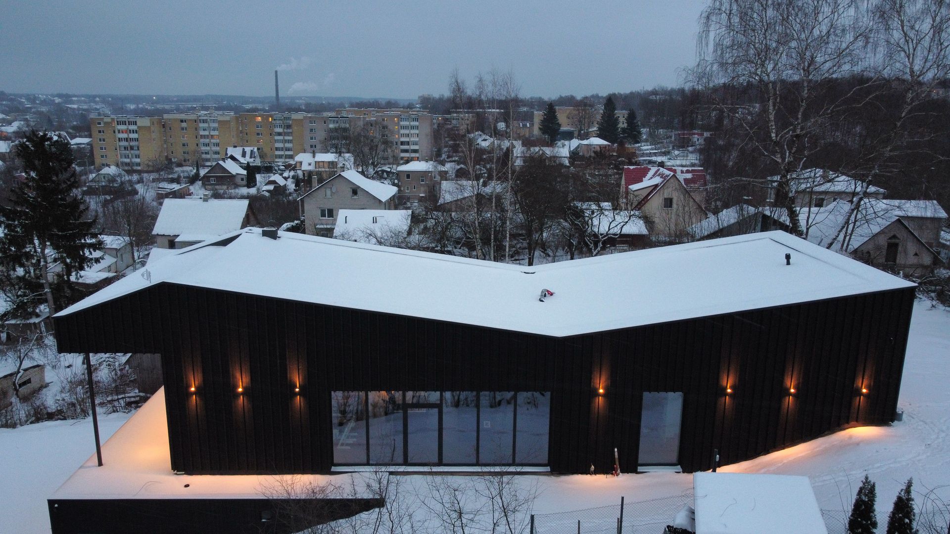 Didelis juodas pastatas su snieguotu stogu yra apsuptas sniegu padengtų medžių.