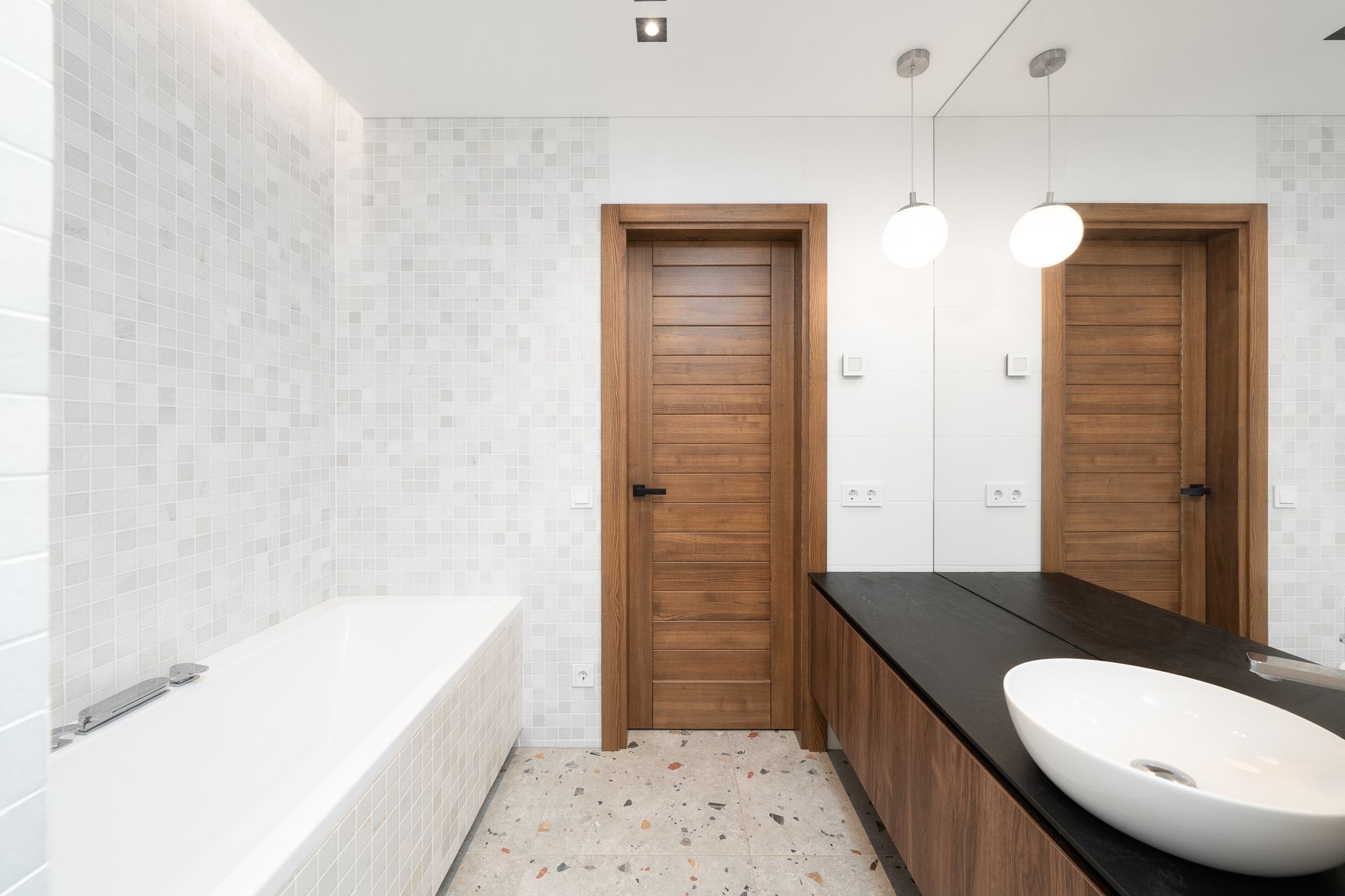 Vonios kambarys su vonia, kriaukle, veidrodžiu ir medinėmis durimis.