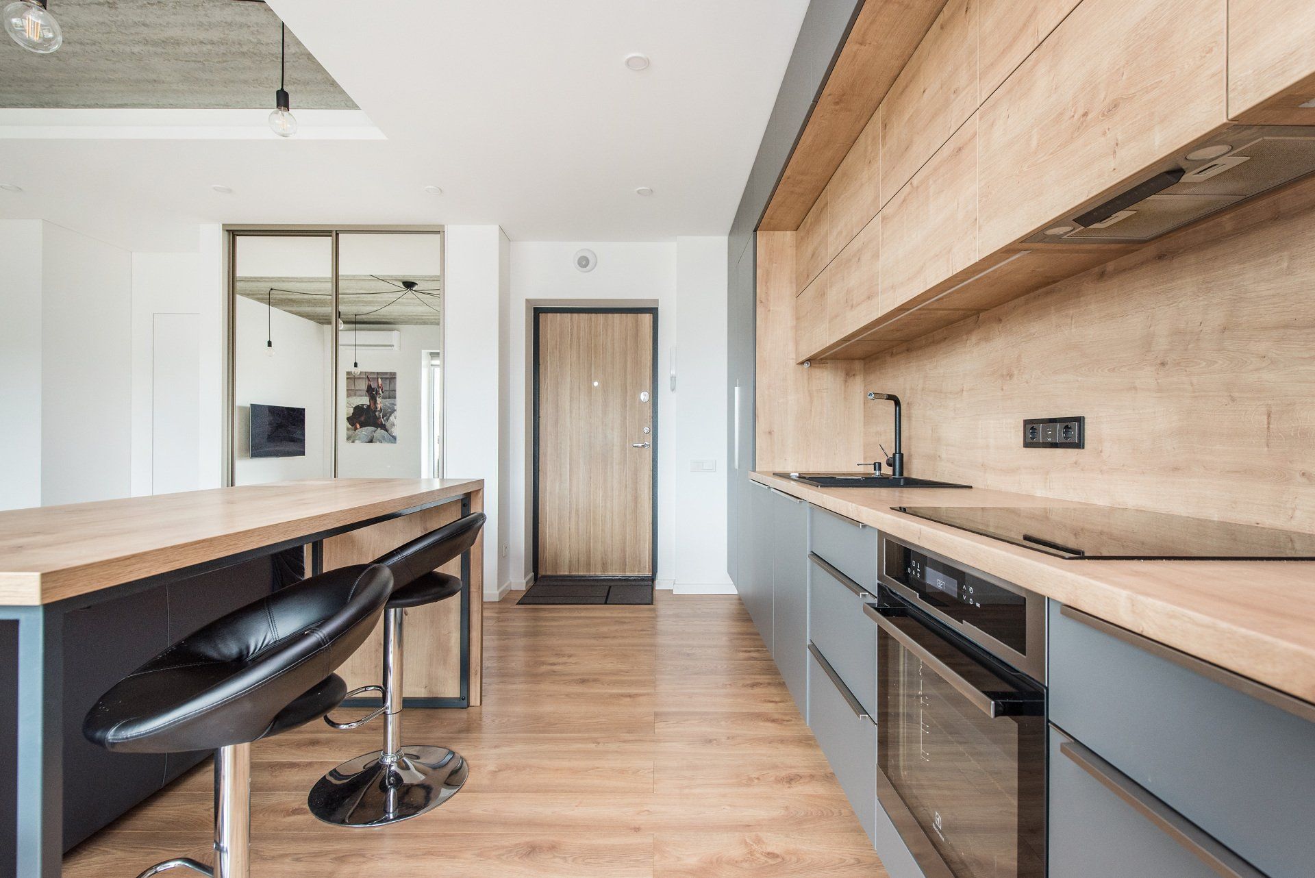 Virtuvė su medinėmis spintelėmis, virykle, kriaukle ir stalu.