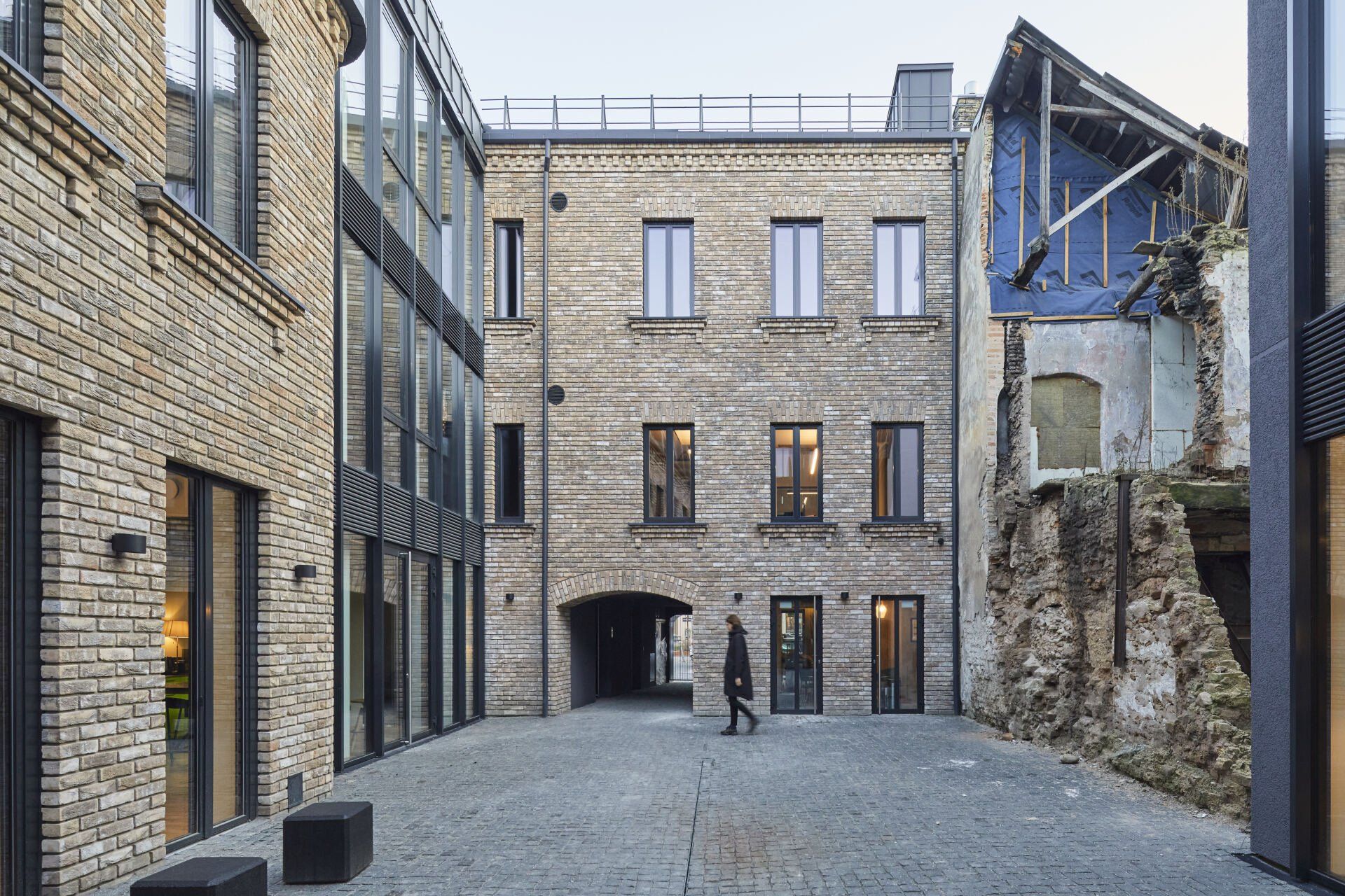 Vyras vaikšto kieme tarp dviejų mūrinių pastatų.