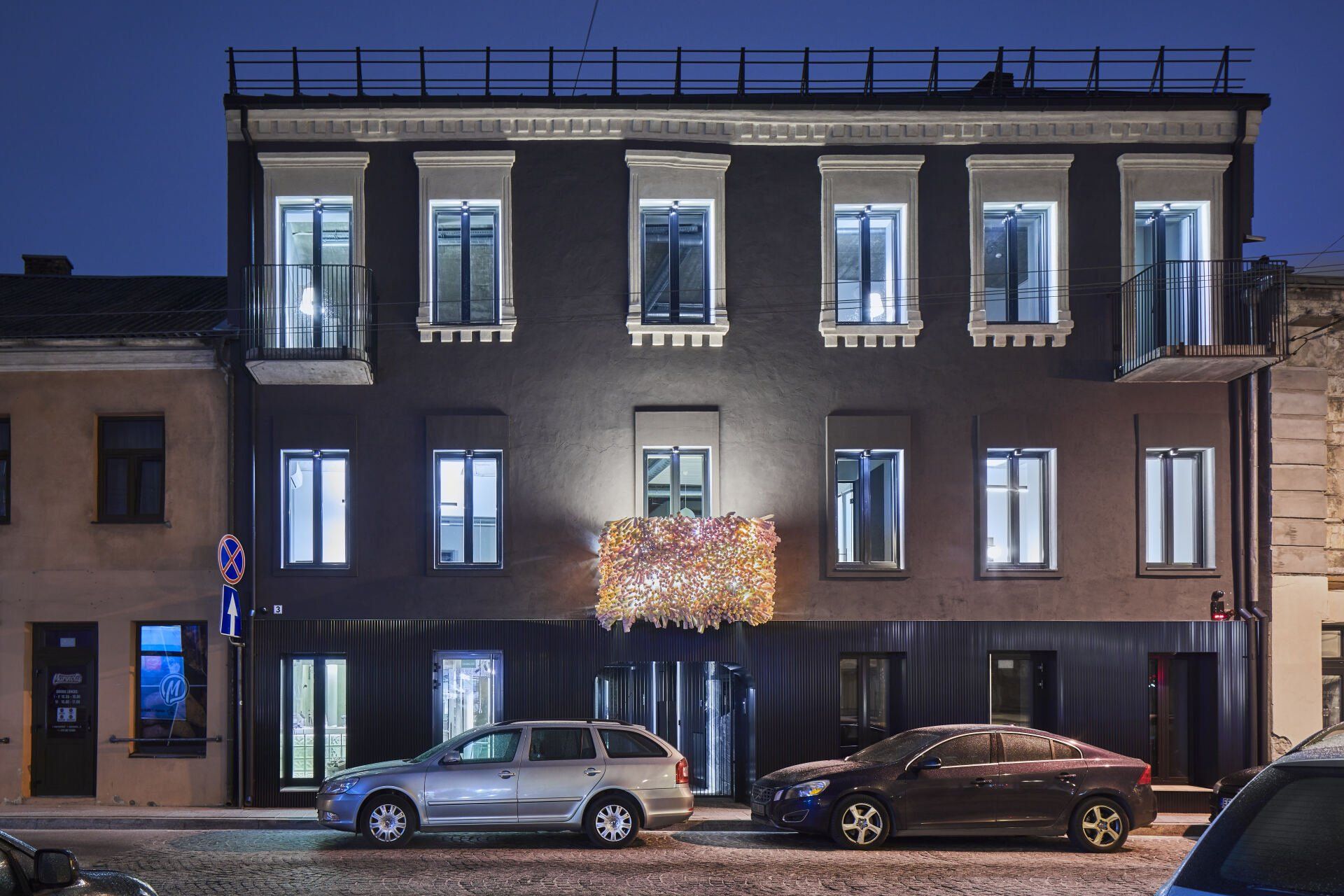 Pastatas, priešais kurį naktį pastatyti automobiliai.