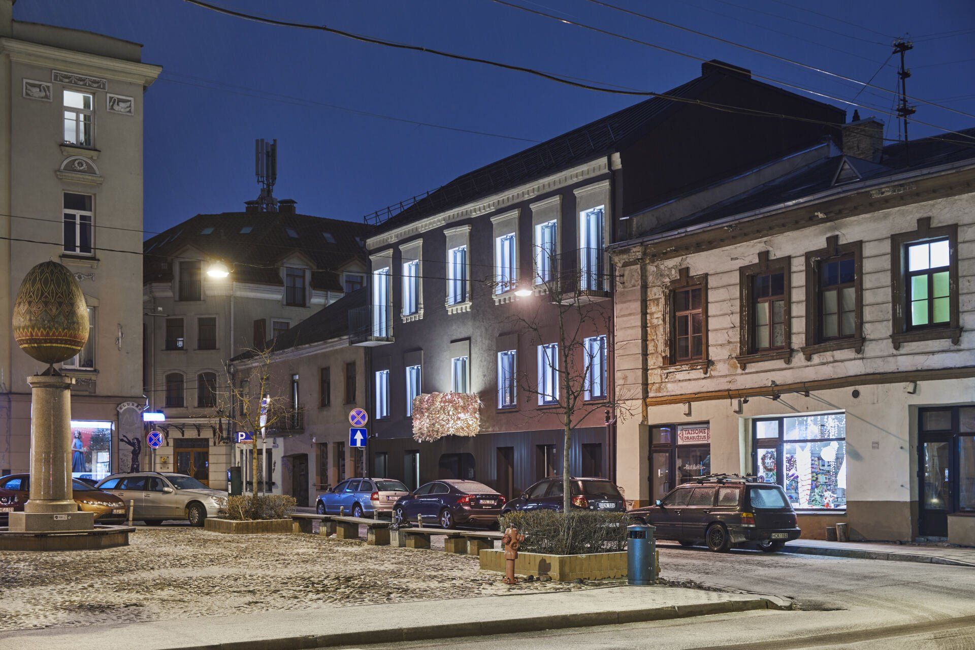 Naktinė miesto gatvė su automobiliais, pastatytais priešais pastatus.