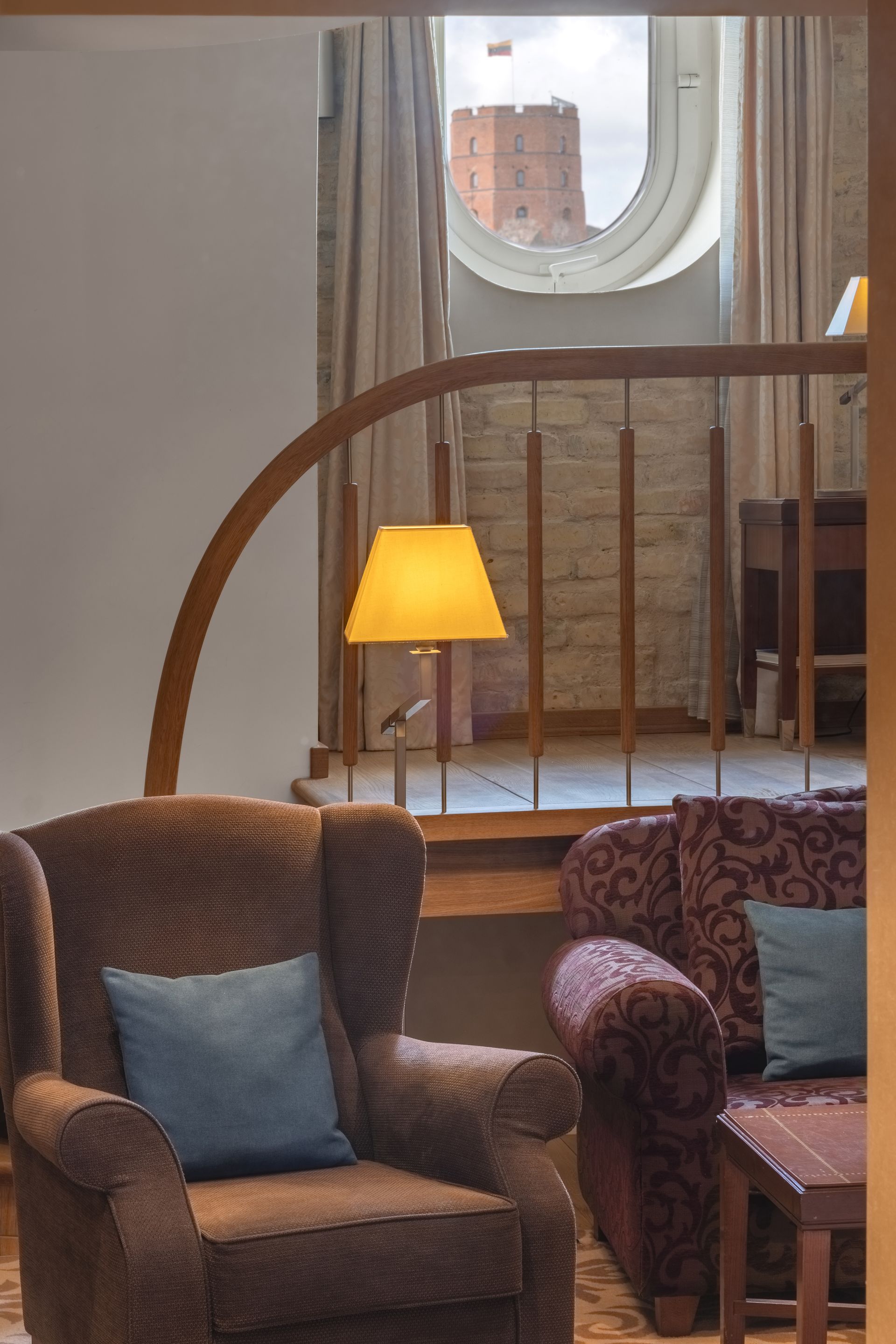 Priešais langą stovi kėdė su mėlyna pagalve