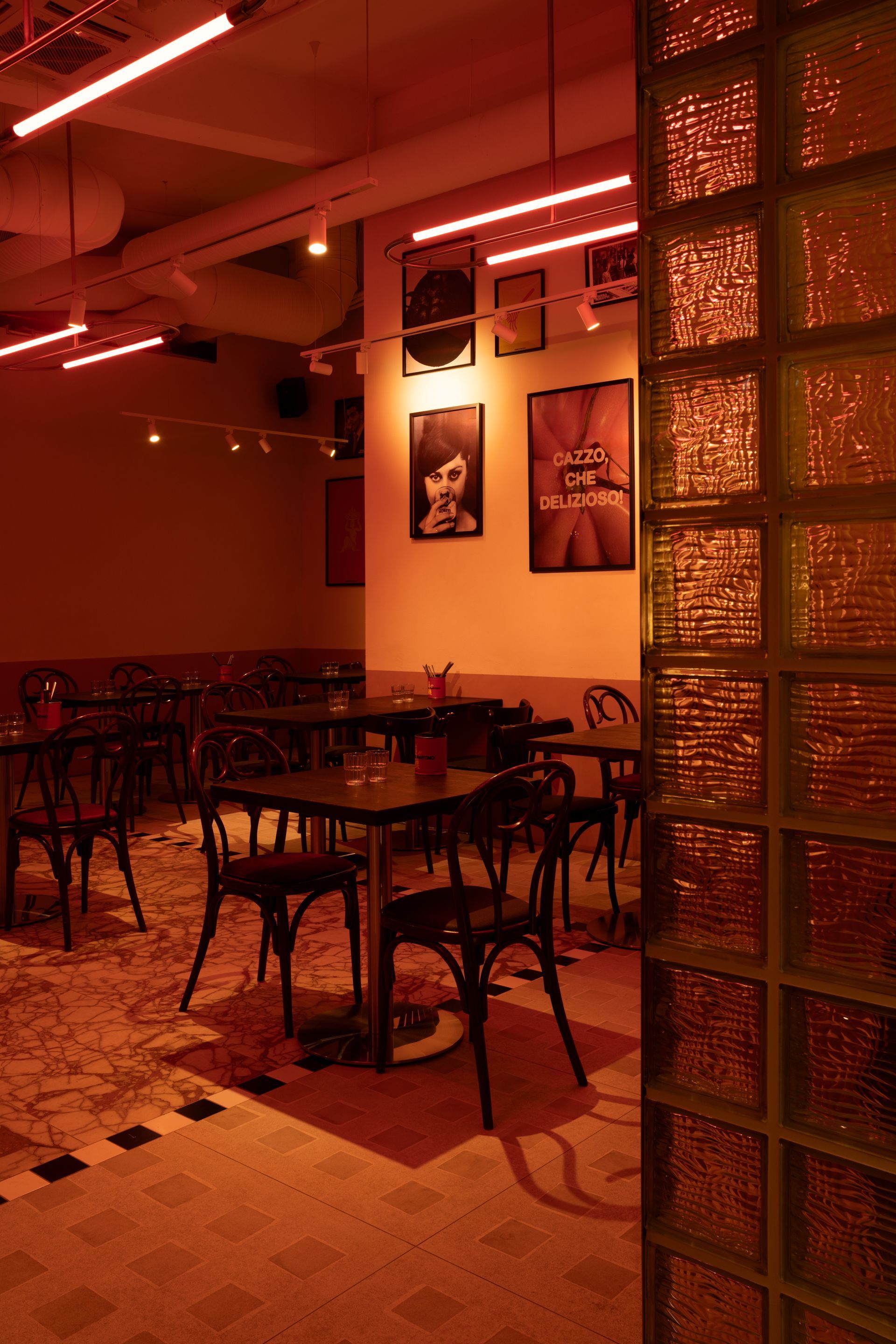 Interior of a cafe with tables and chairs, illuminated with orange lighting and posters on the wall.