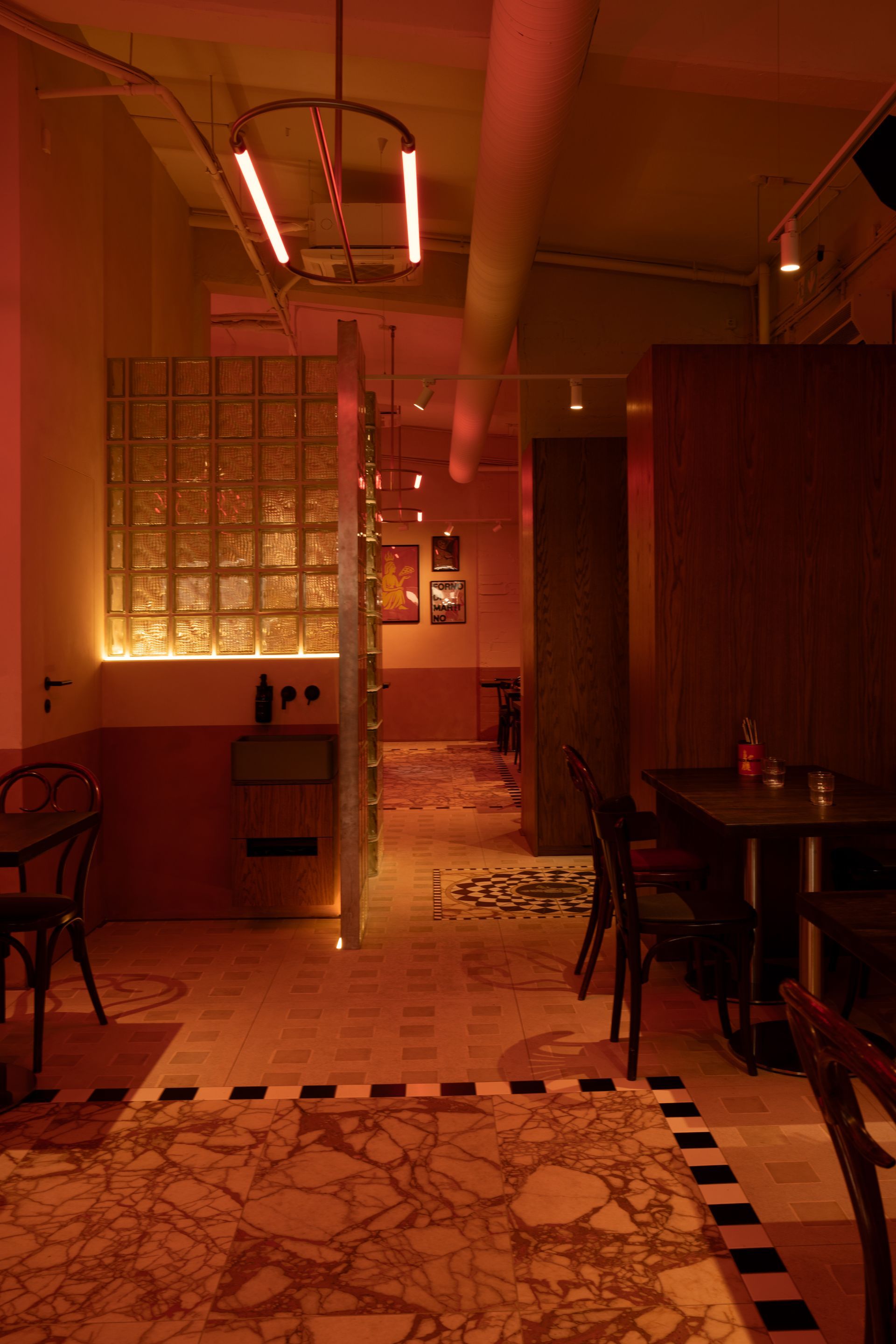Restaurant interior with patterned tile floor, red lighting, glass block wall, and tables.