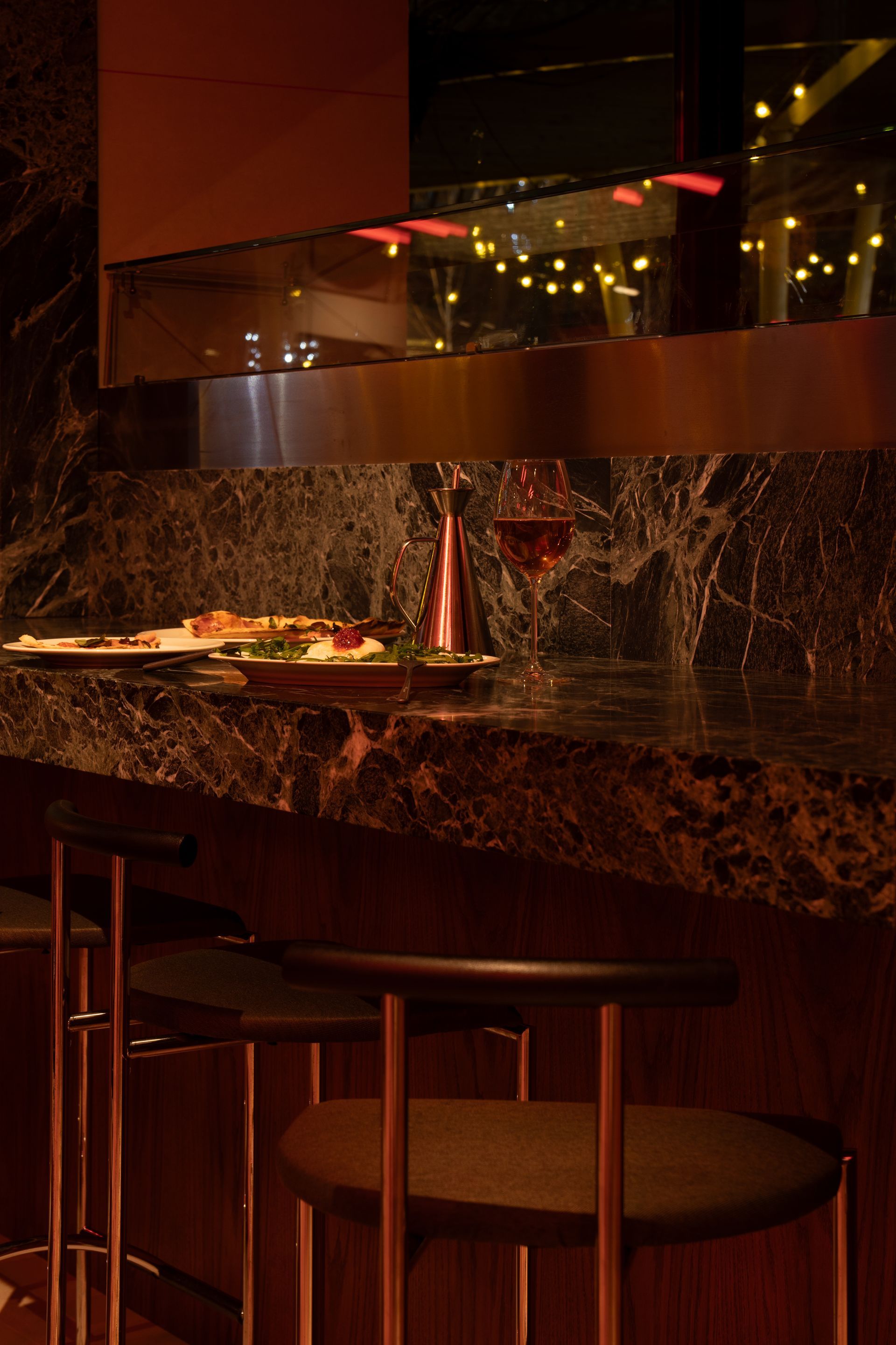 Bar with marble counter, stools, and drinks, reflected in a mirror. Warm lighting.