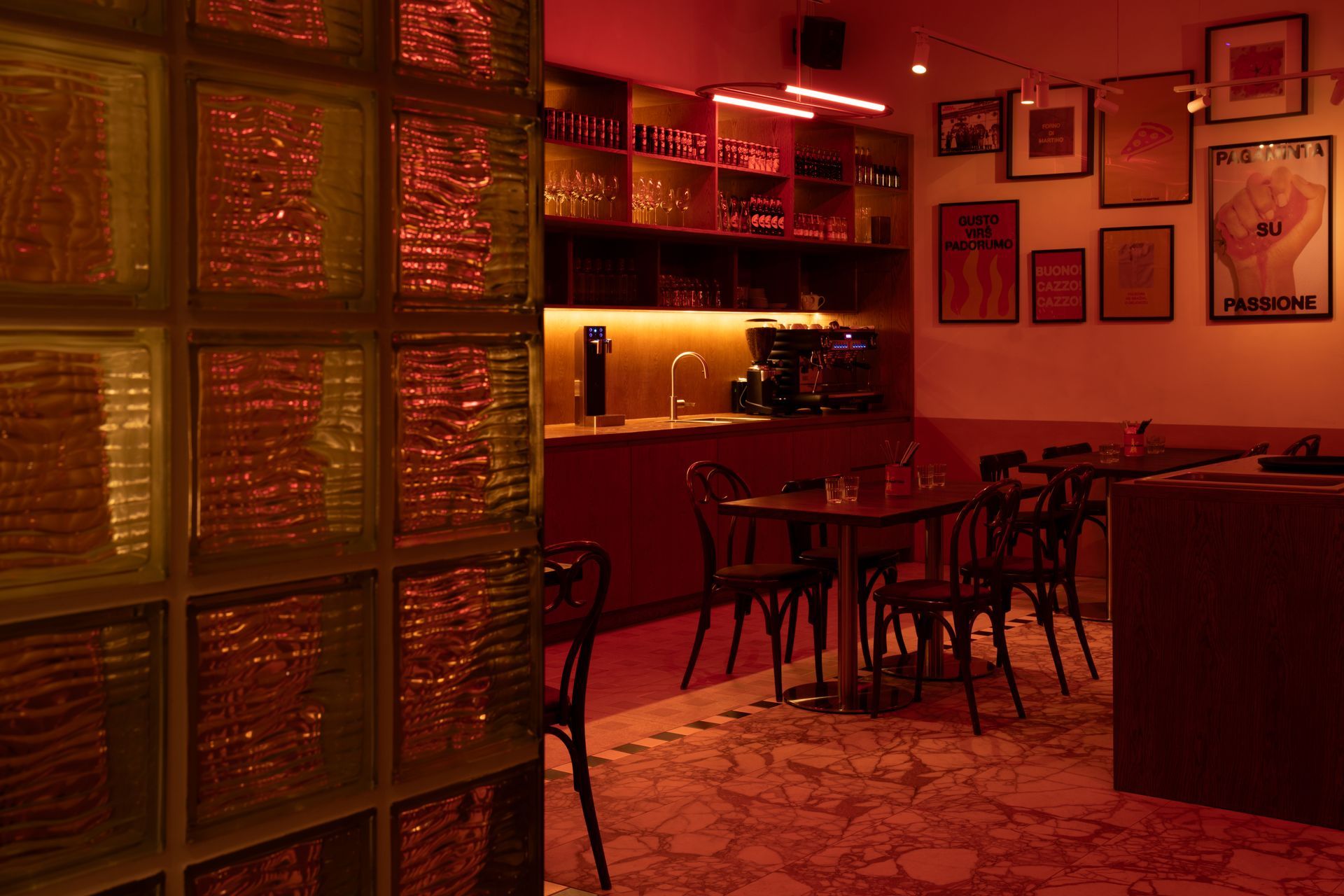 Restaurant interior with a red ambiance.  A glass block wall is in the foreground. Tables, chairs, and decor are visible.