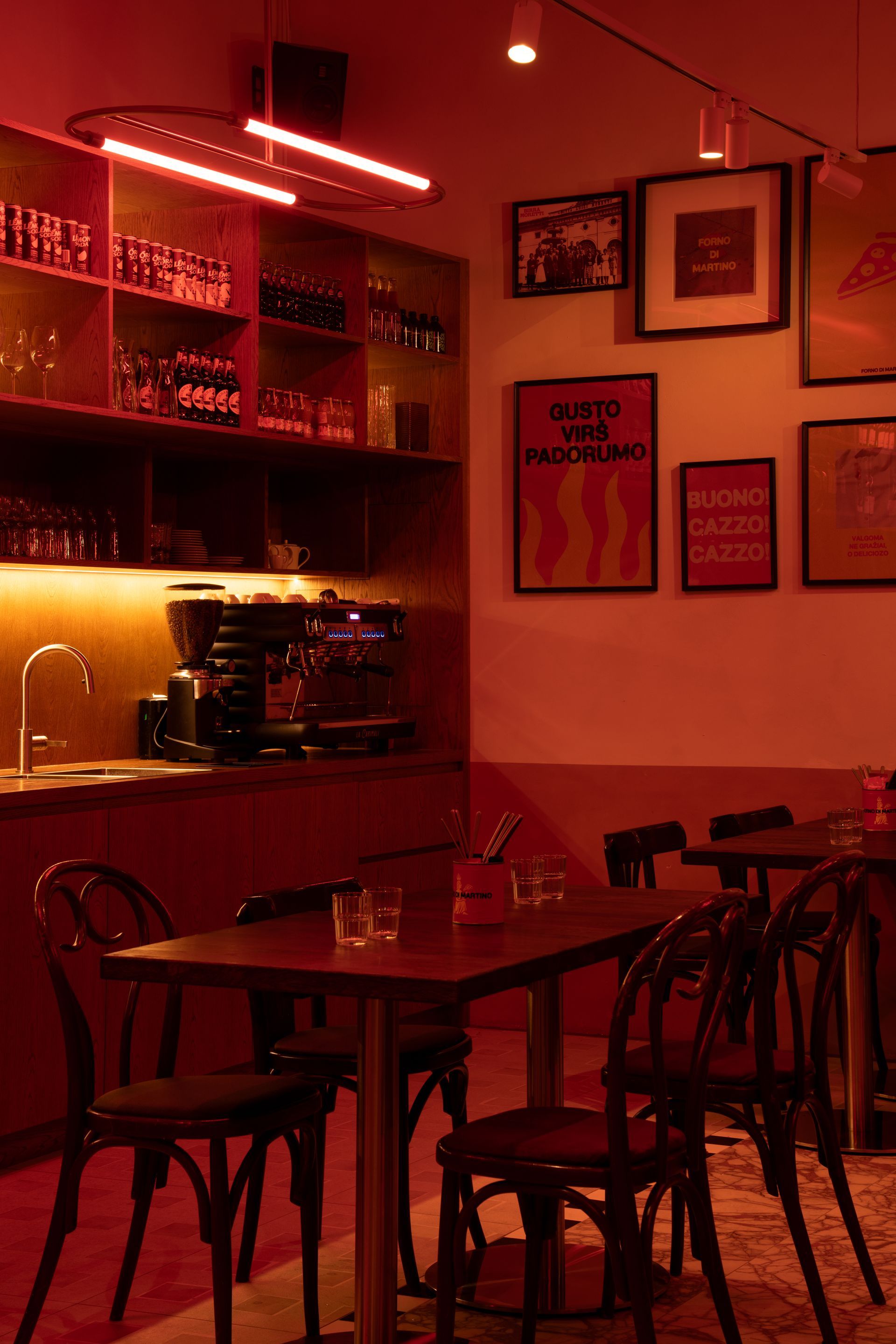 Red-lit interior of a restaurant with tables, chairs, bar area, and framed art on the walls.