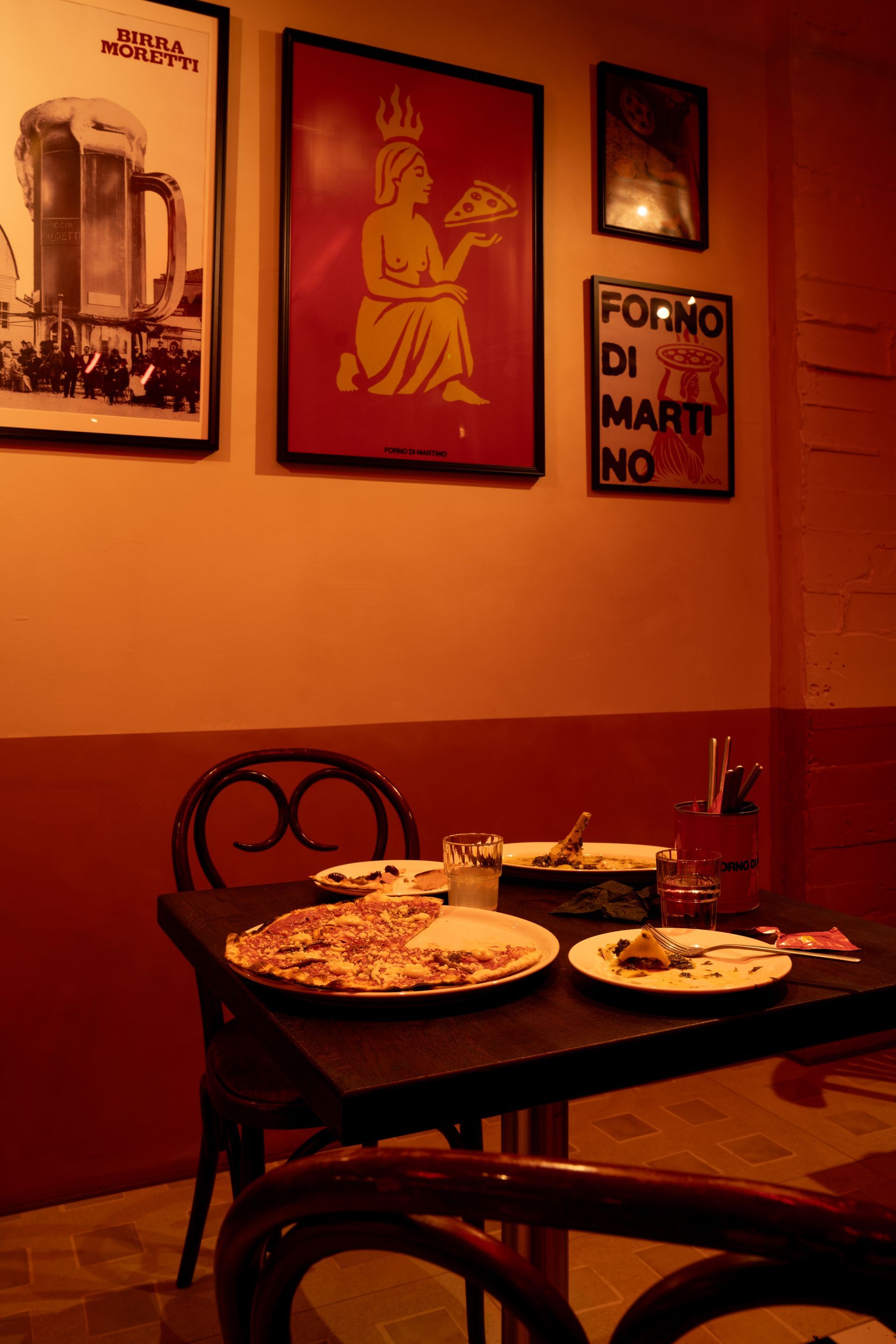 Table with pizza crusts, in a restaurant with posters on the wall; reddish-orange color scheme.