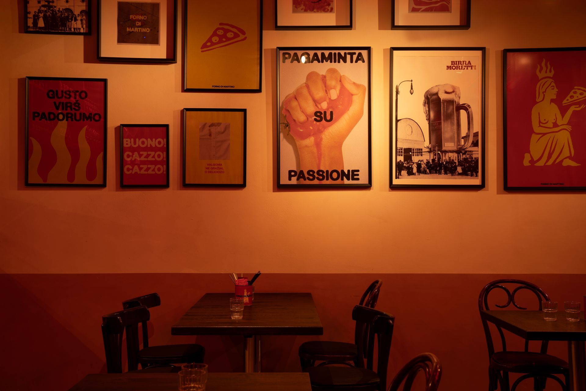 Restaurant interior with tables, chairs, and posters on the wall, lit with warm lighting.