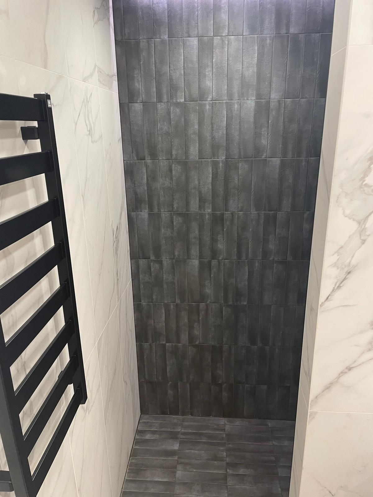 Vonios kambarys su juodomis plytelėmis ir juoda rankšluosčių kabykla.